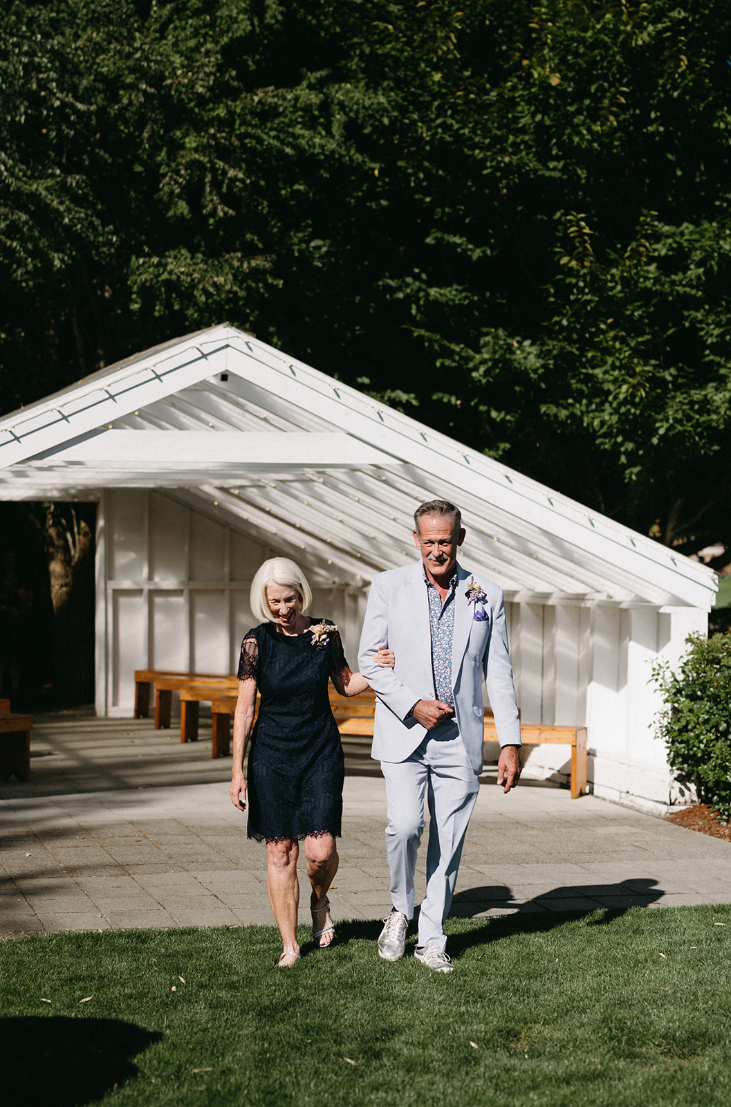 Bride's parents walking arm in arm from modern white structure