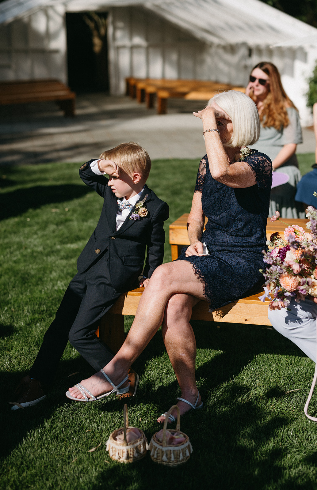 Child and grandma shielding eyes from sun while seated at wedding ceremony