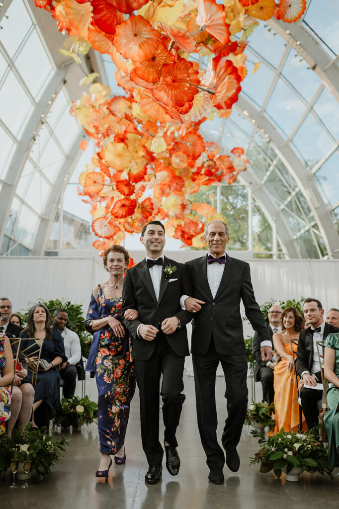 Groom walking down the aisle with his parents at Chihuly Garden and Glass — a unique Seattle wedding ceremony venue