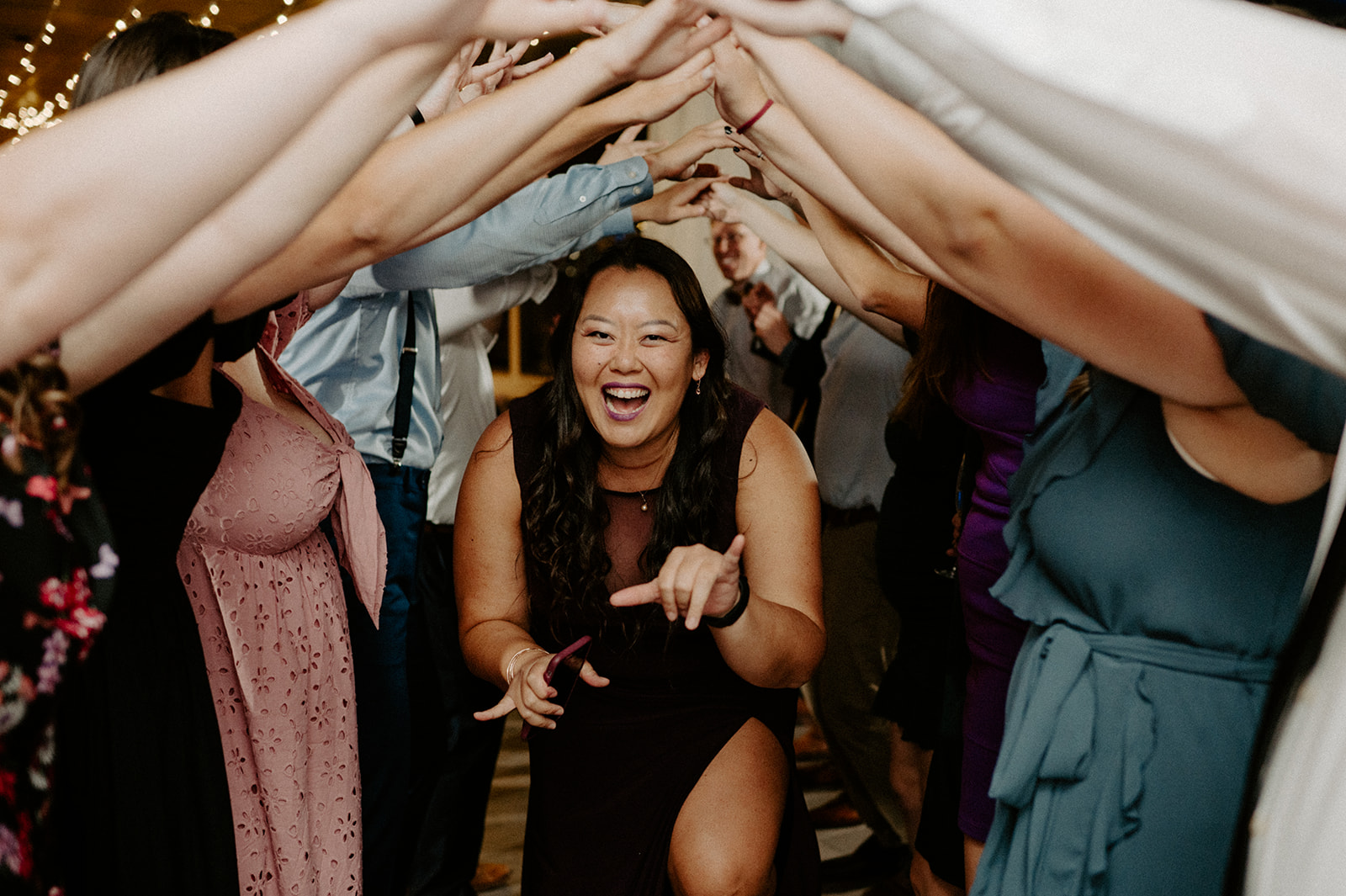 A guest enjoying the reception, smiling while dancing under an arch of hands made by other wedding guests.