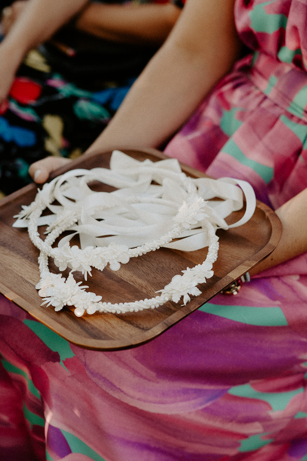 A guest holding a wooden tray with delicate floral crowns during an outdoor wedding ceremony.