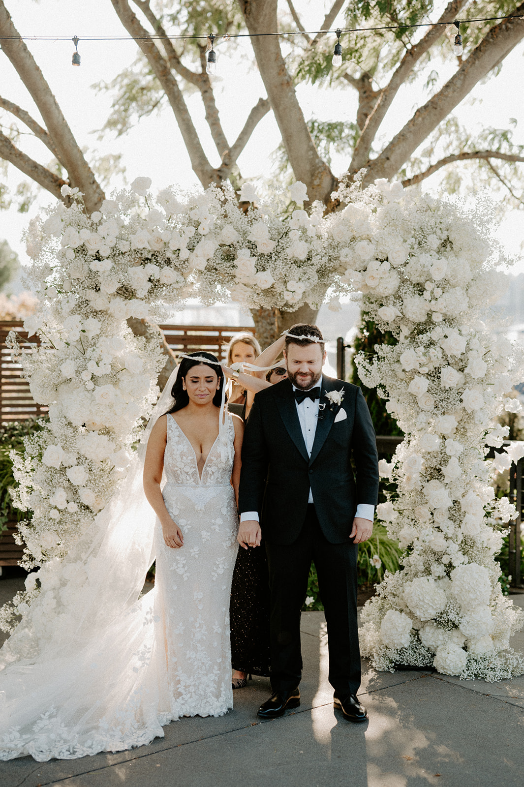 The couple stands hand in hand under a floral arch during their outdoor wedding ceremony.