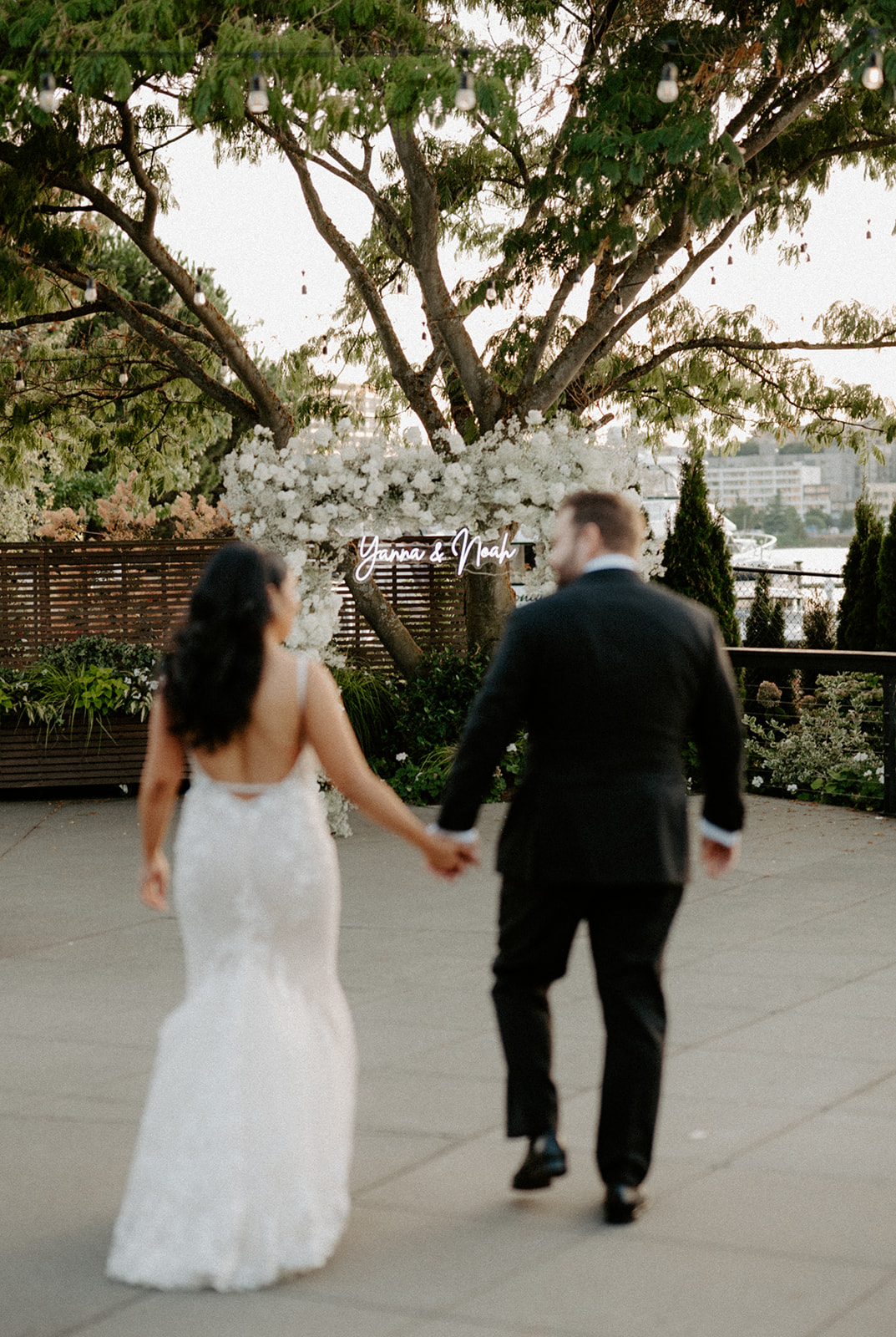 Bride and groom walking hand-in-hand past a personalized floral arch at Dockside at Duke’s.