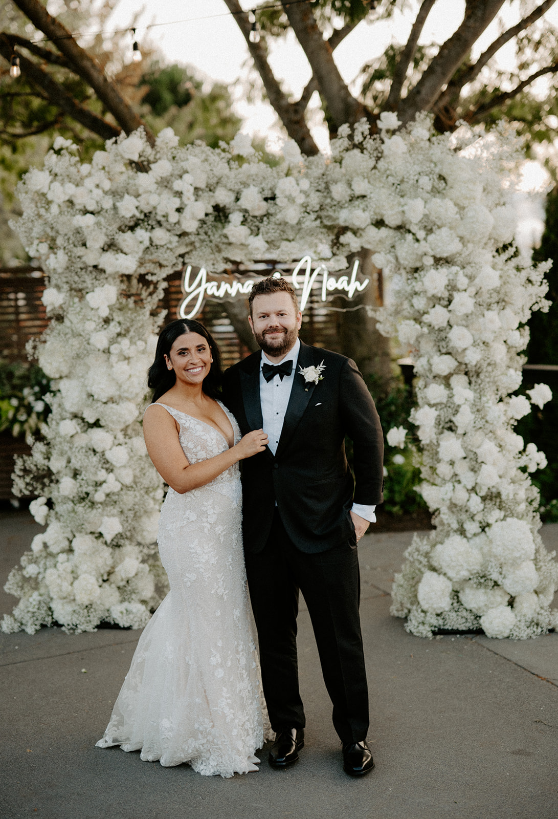 Bride and groom posing in front of a floral arch at Dockside at Duke’s wedding.