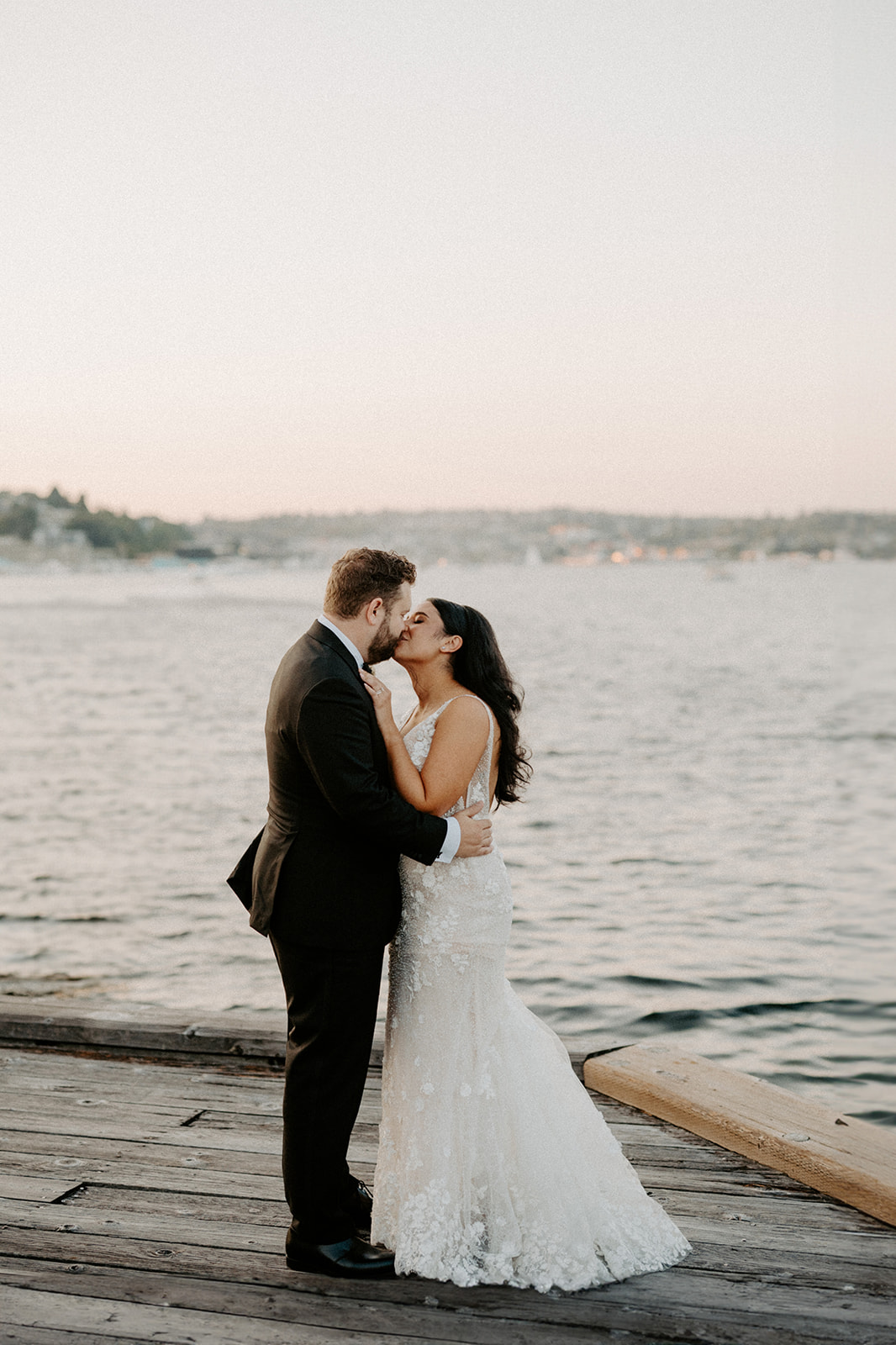 Bride and groom sharing a kiss on a dock with the Seattle skyline in the background.