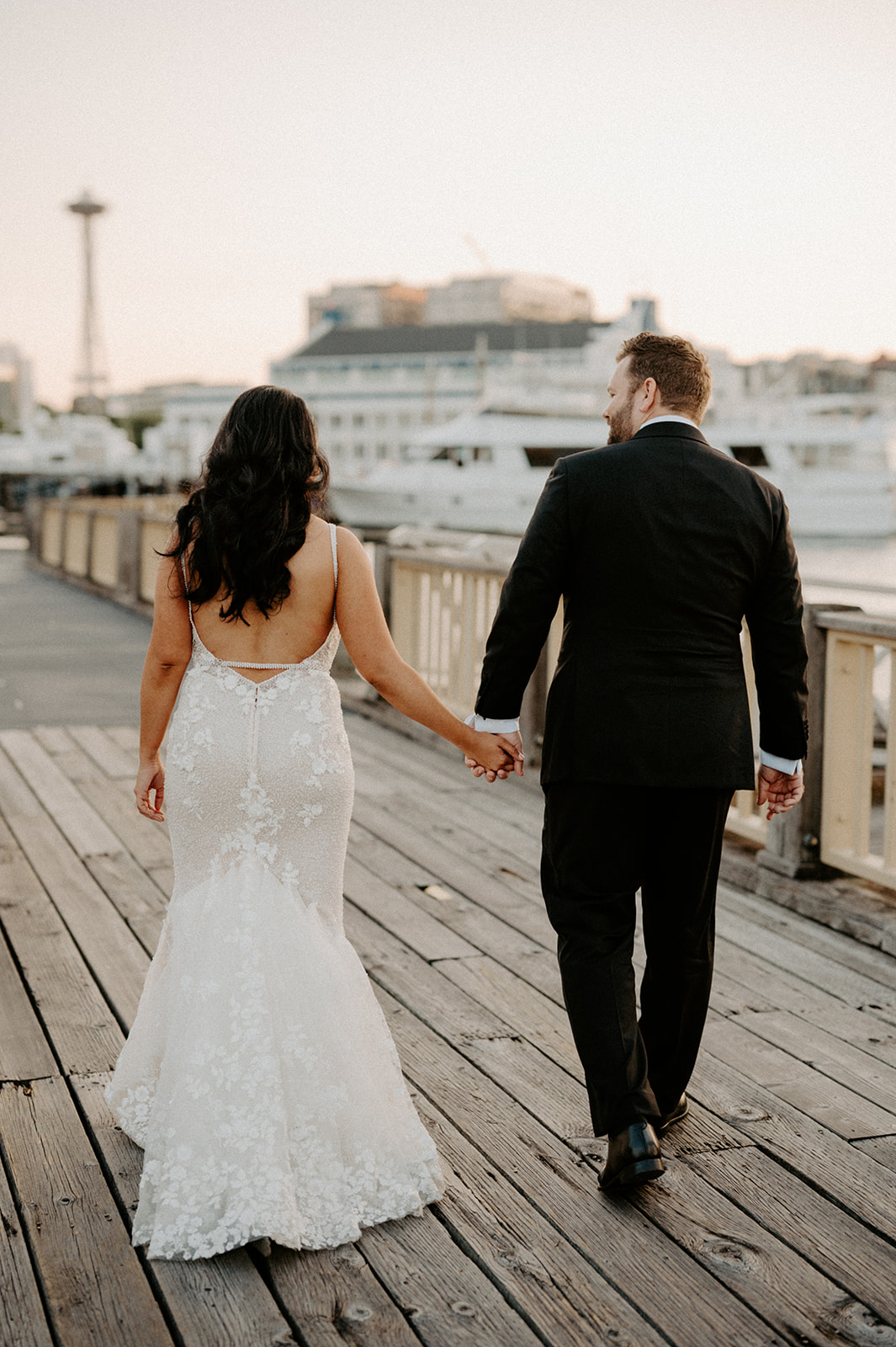 Bride and groom walking hand-in-hand along a dock with the Seattle Space Needle in the background.