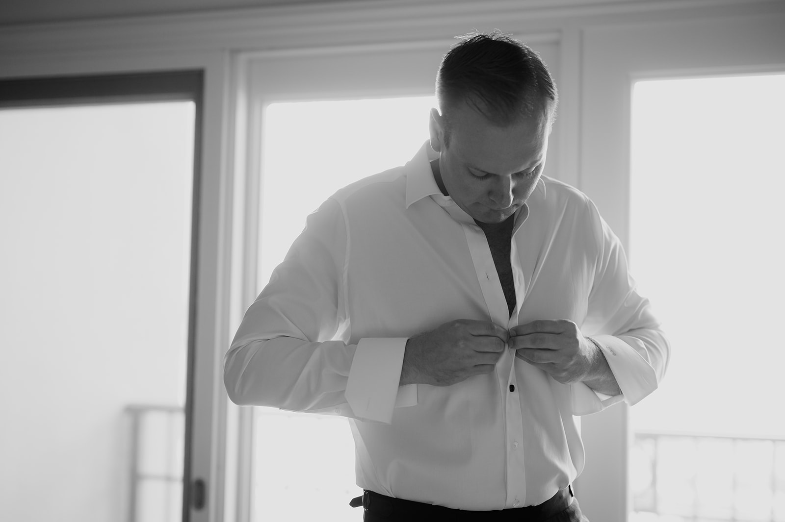 Black and white photo of the groom buttoning his dress shirt in his hotel room in Maui.
