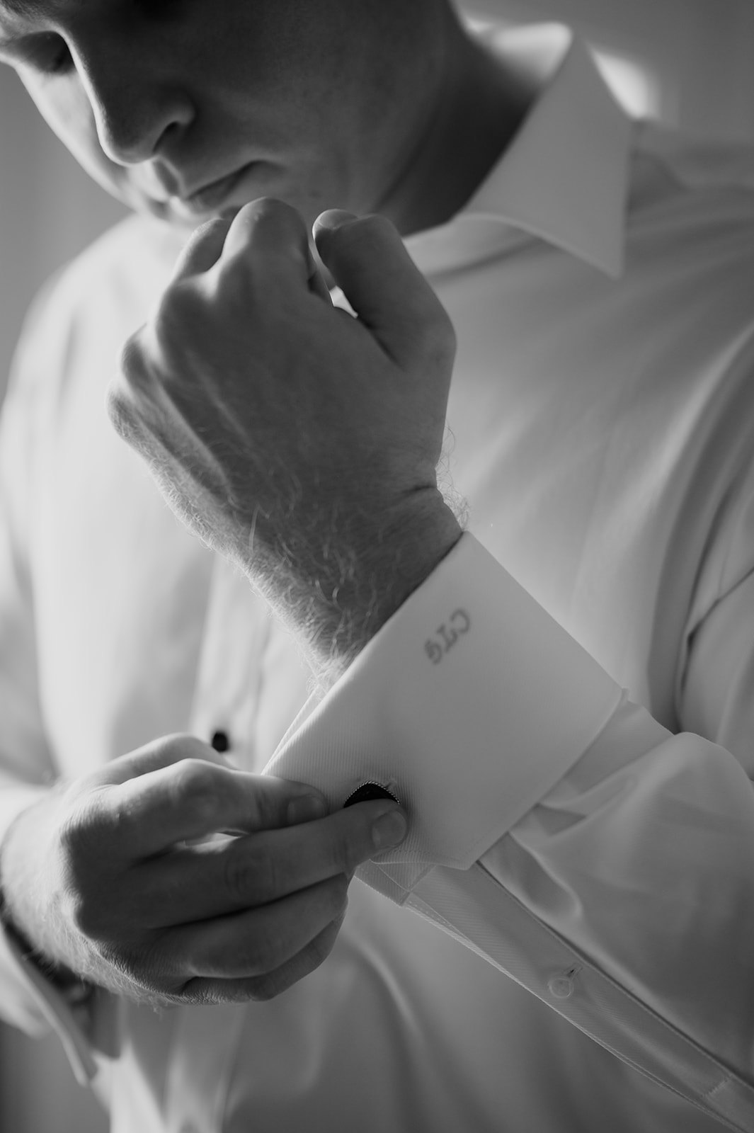 Black and white close-up of the groom fastening his cufflink on a white dress shirt while getting ready in Maui.
