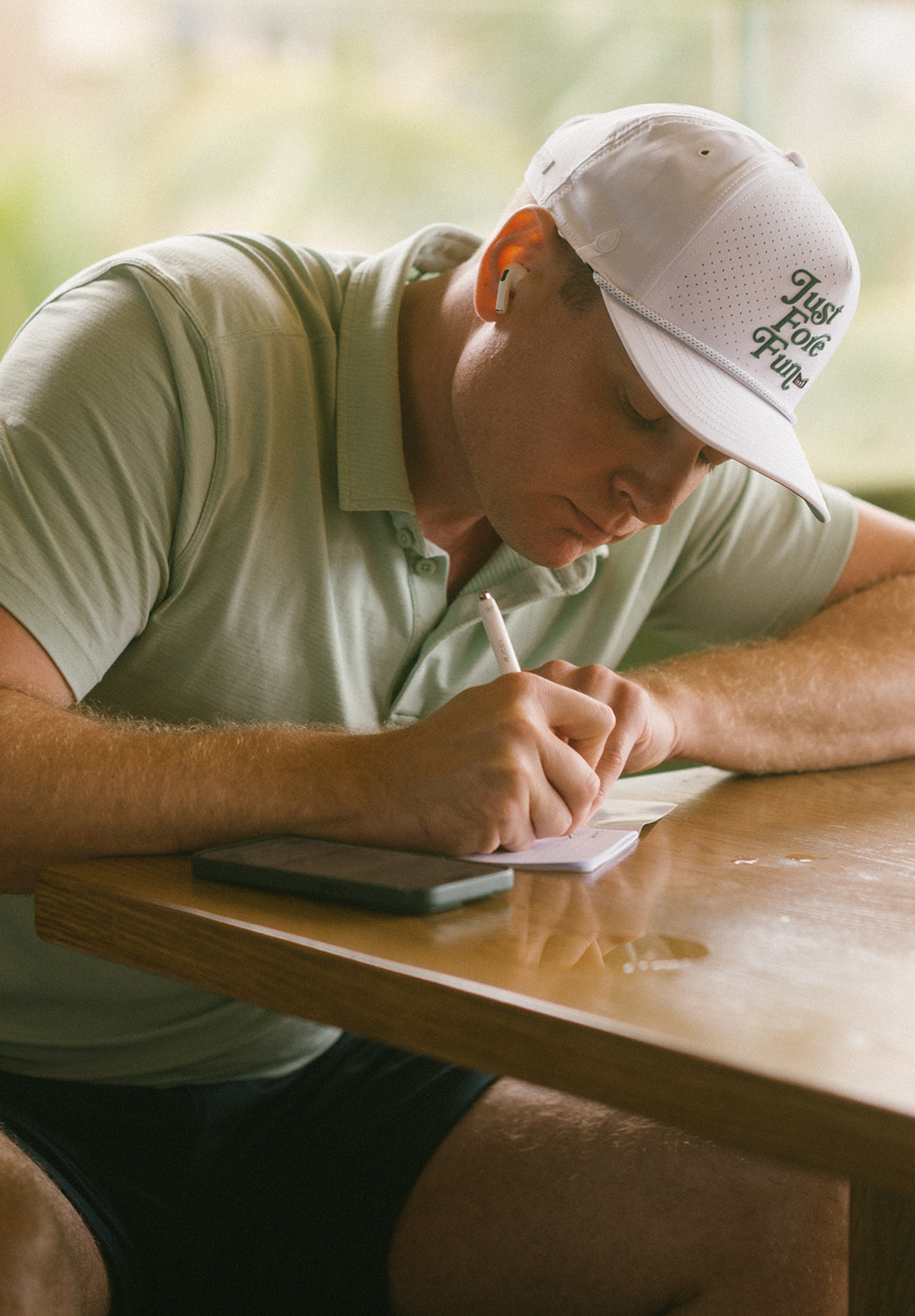 Close-up of the groom’s hands writing vows in a notebook at a wooden table.
