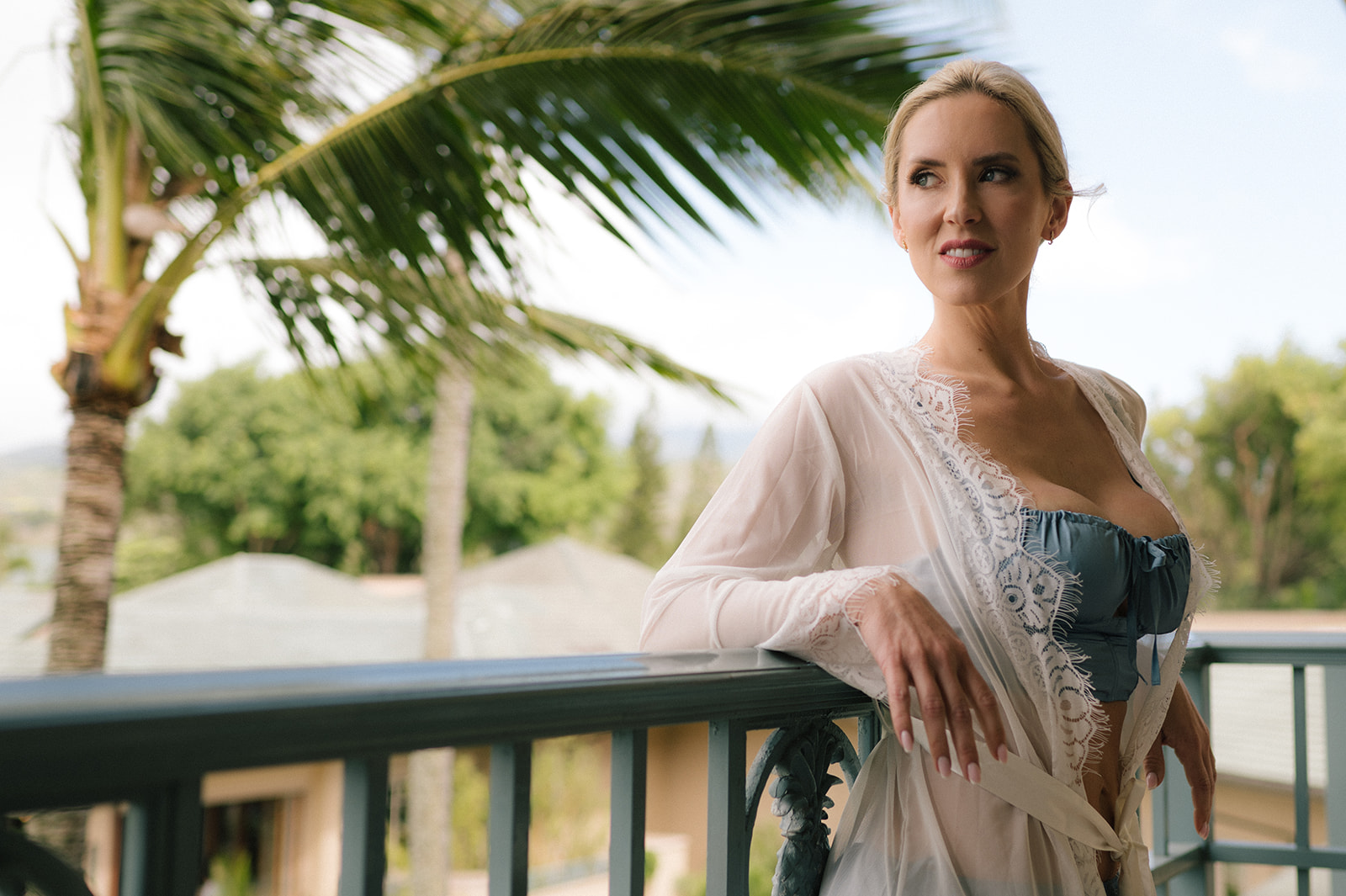 Bride standing on a balcony in her robe overlooking palm trees and tropical scenery in Maui.
