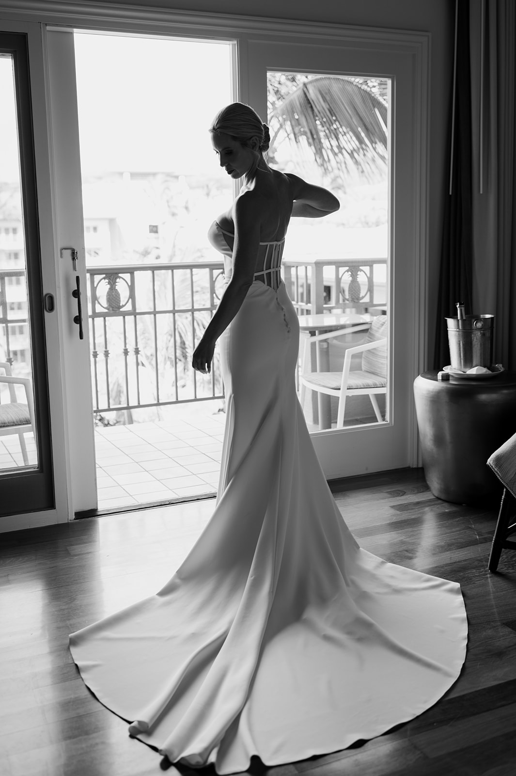Black and white silhouette of the bride standing in her wedding dress near the balcony doors in Maui.

