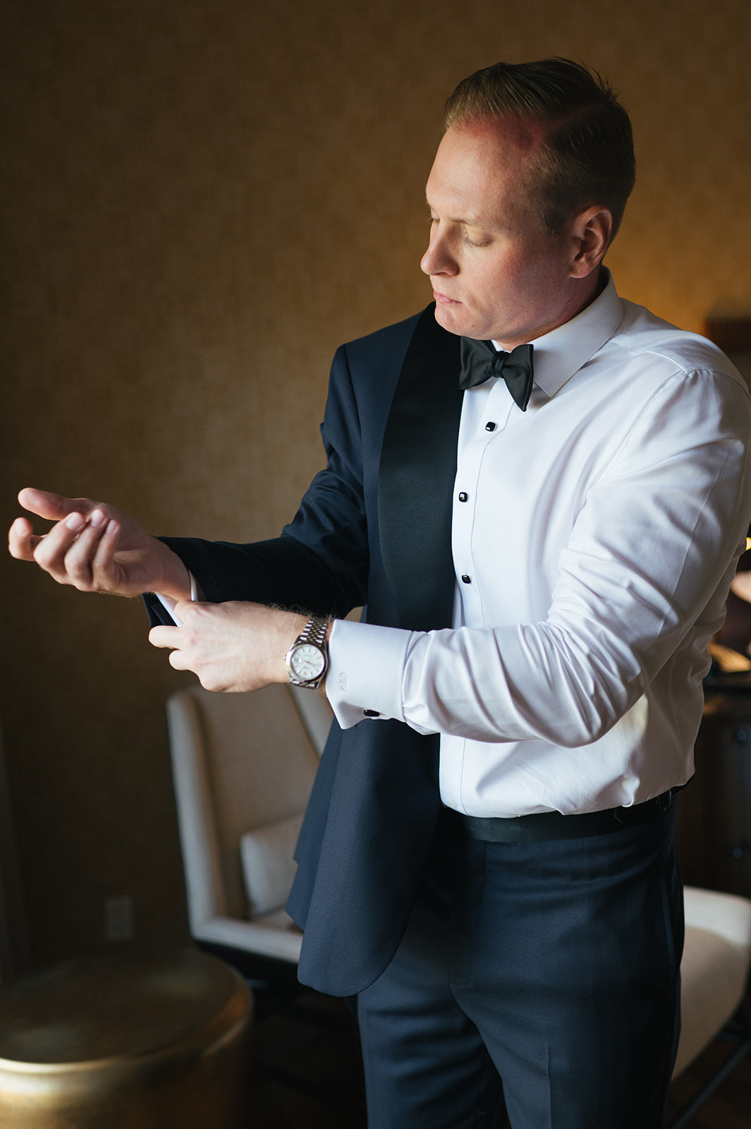 Groom fastening his cufflinks while wearing a tuxedo during wedding preparations in Maui.
