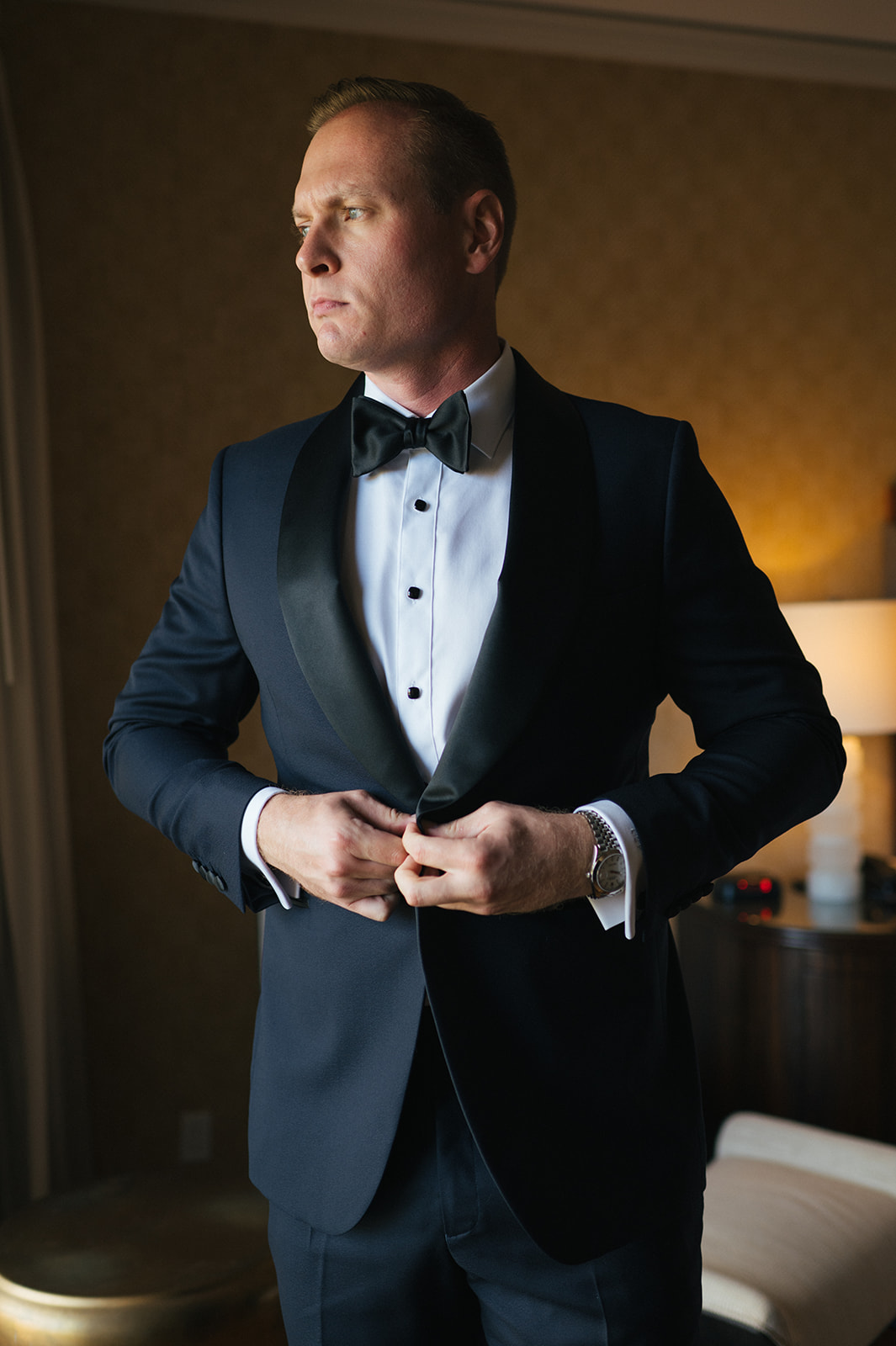 Groom buttoning his tuxedo jacket in soft window light at the Four Seasons Maui.
