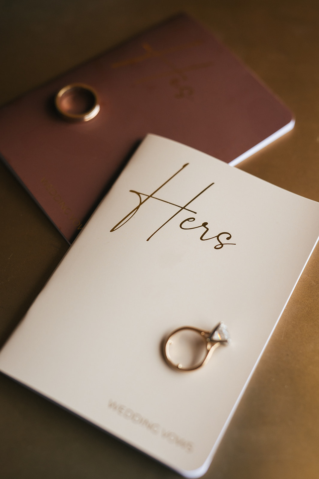 Diamond engagement ring resting on a wedding vows booklet labeled “Hers.”
