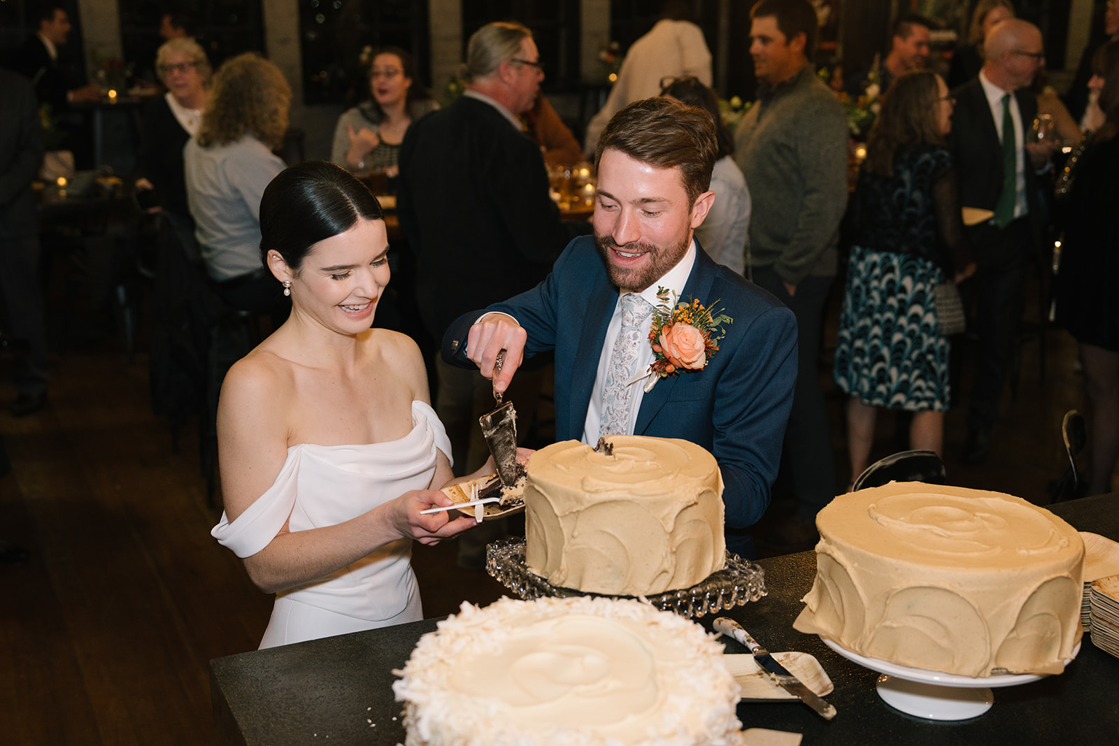 Bride and groom laugh while cutting their wedding cake.