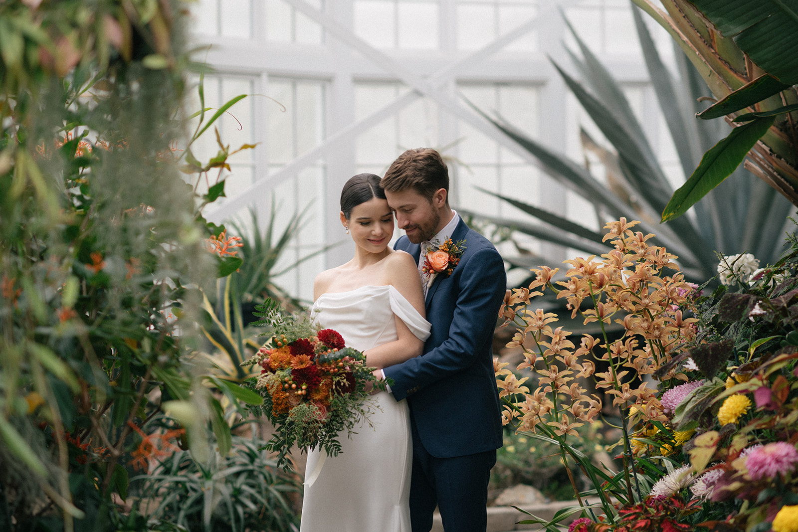 Patrick embraces Taylor as they share an intimate moment surrounded by tropical plants and vibrant blooms.