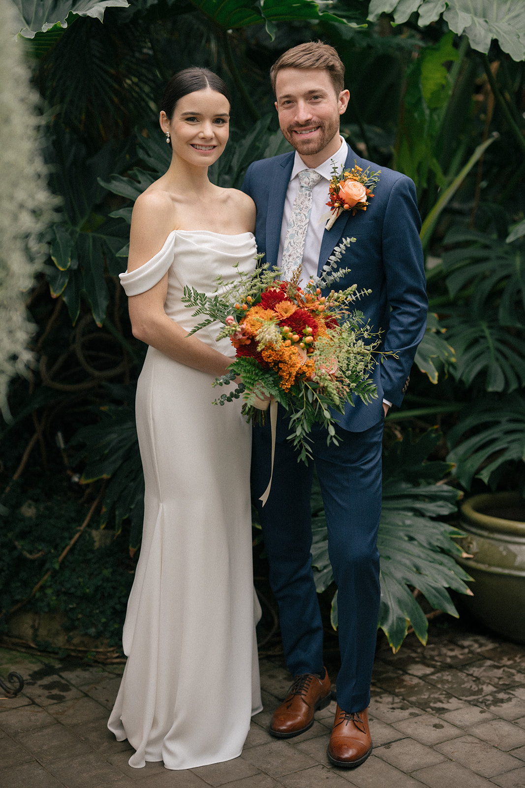 Taylor and Patrick smiling with vibrant florals and lush greenery in the Seymour Conservatory.