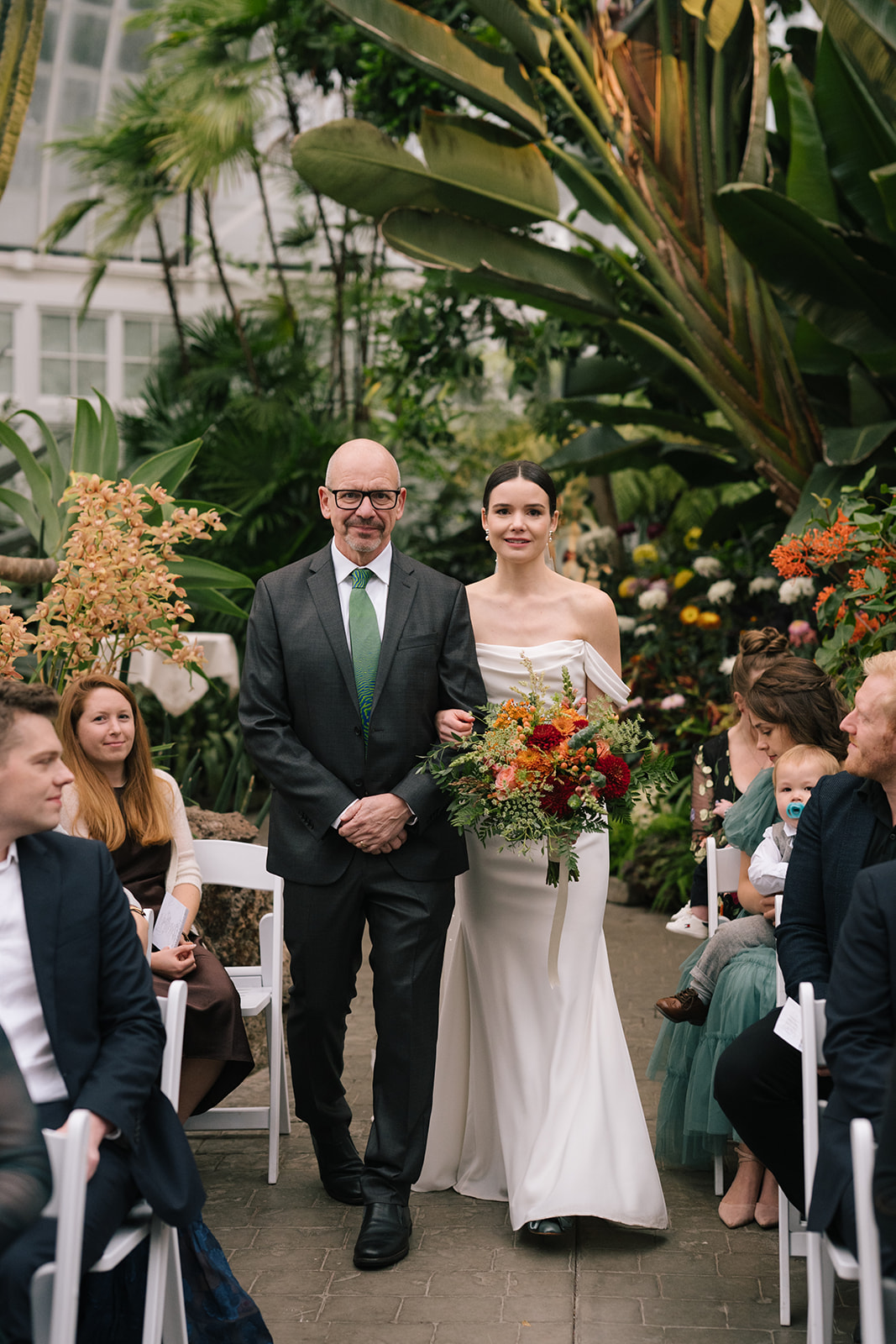 Taylor walking down the aisle arm-in-arm with her father, holding a vibrant bouquet.