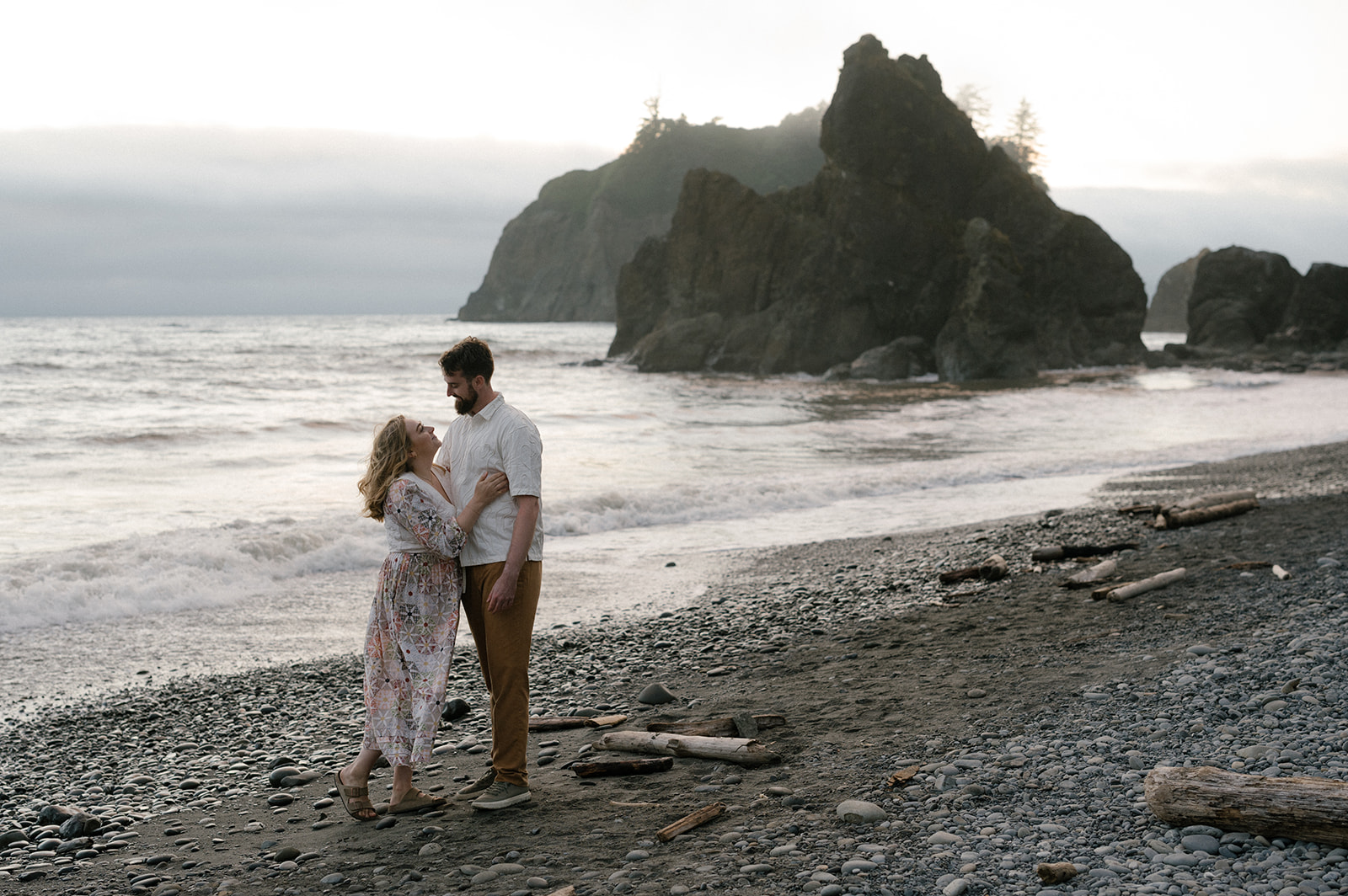 Couple embracing on Ruby Beach with dramatic sea stacks rising from the ocean behind them, Olympic National Park Washington