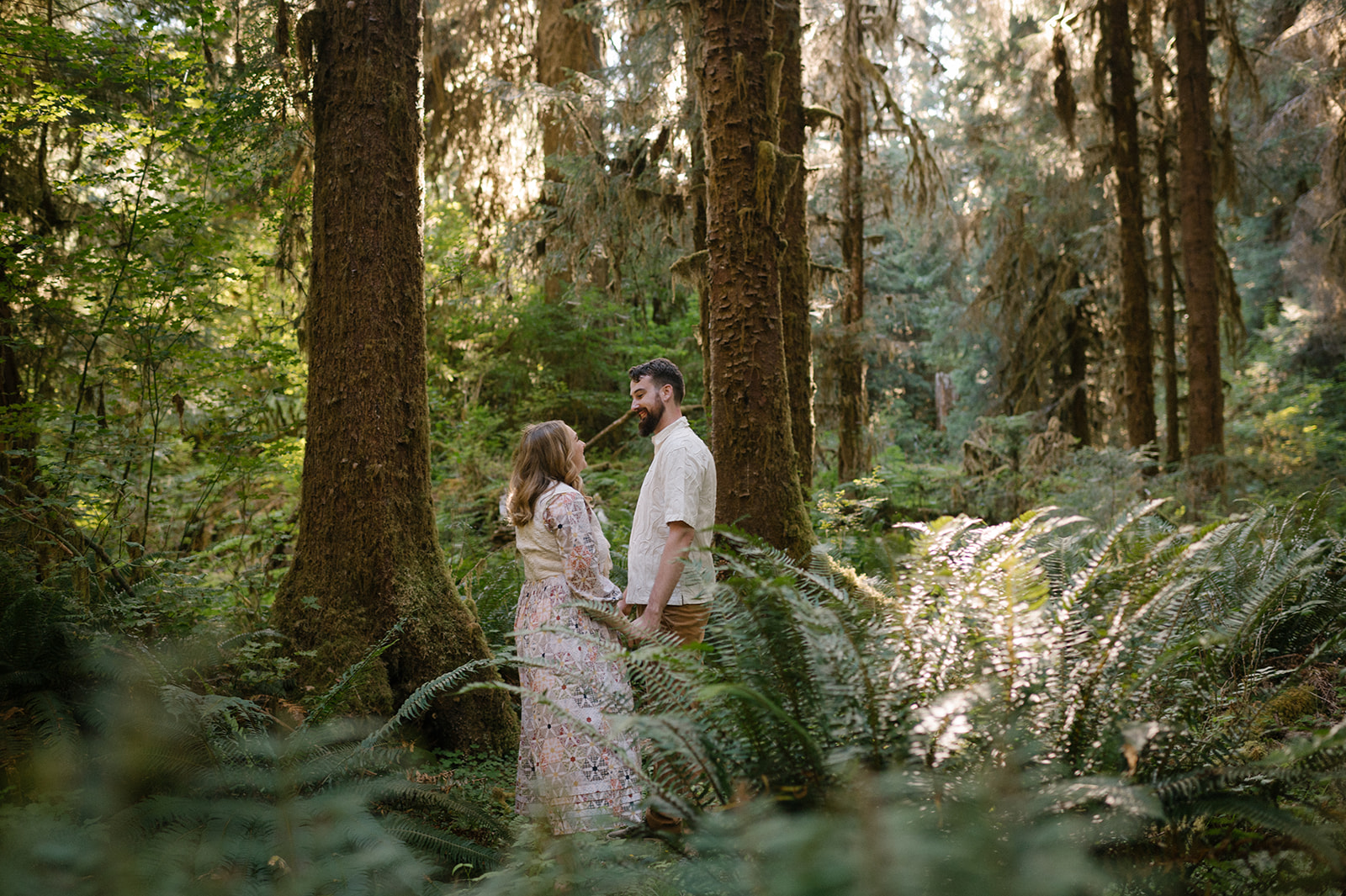 Couple standing face to face surrounded by ferns and moss-covered trees in the Hoh Rainforest, one of the best places to elope on the Washington Coast, Olympic National Park