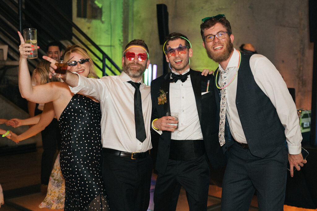 Wedding guests wearing fun sunglasses and dancing with drinks at the Fremont Foundry reception