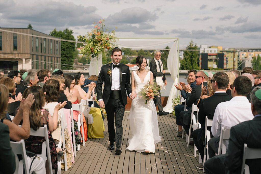 Bride and groom walking back down the aisle as guests applaud during their Fremont Foundry rooftop ceremony