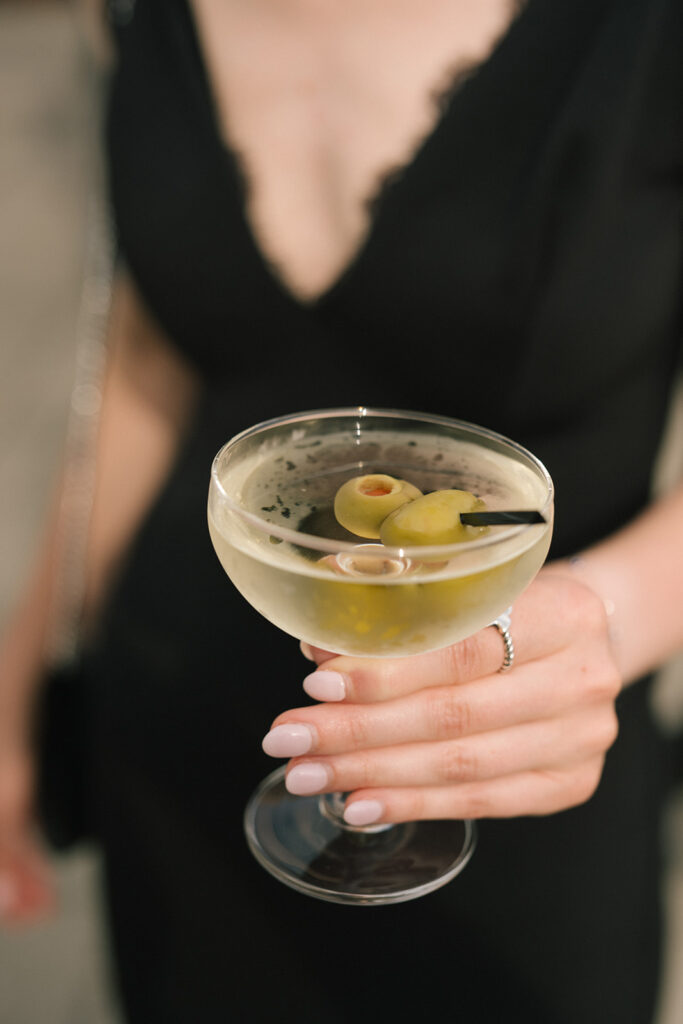 Close-up of a martini with olives held by a guest during cocktail hour at a Fremont Foundry wedding