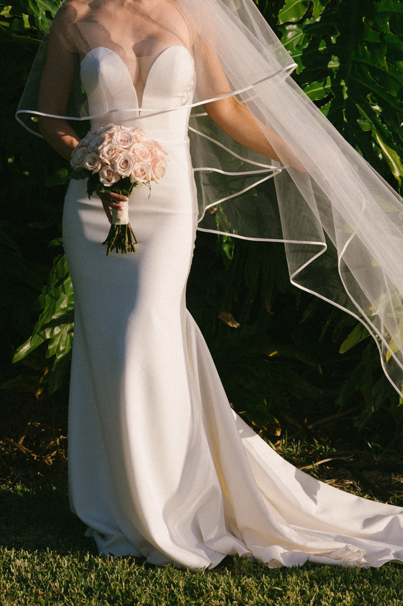 Bride holding a blush rose bouquet with her veil flowing in tropical greenery at Merriman’s Kapalua in Maui.