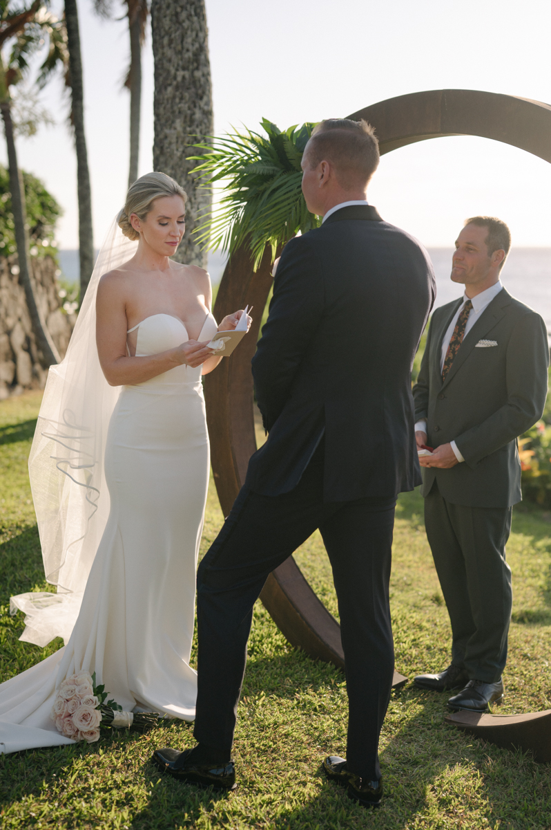 Bride reading her vows to the groom during their ceremony at Merriman’s Kapalua with the ocean behind them.
