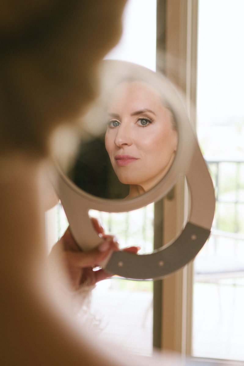 Bride looking at her reflection in a handheld mirror while getting ready in her suite at the Four Seasons Maui.
