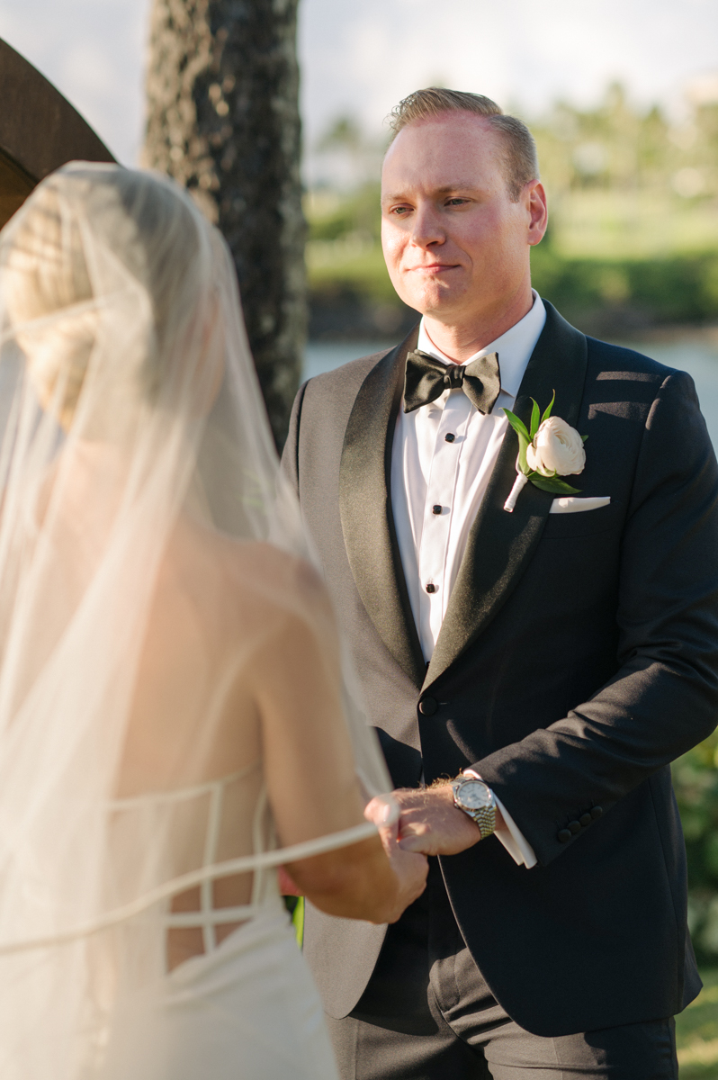 Groom listening to the bride’s vows as they stand beneath a tropical arch overlooking the ocean in Kapalua.

