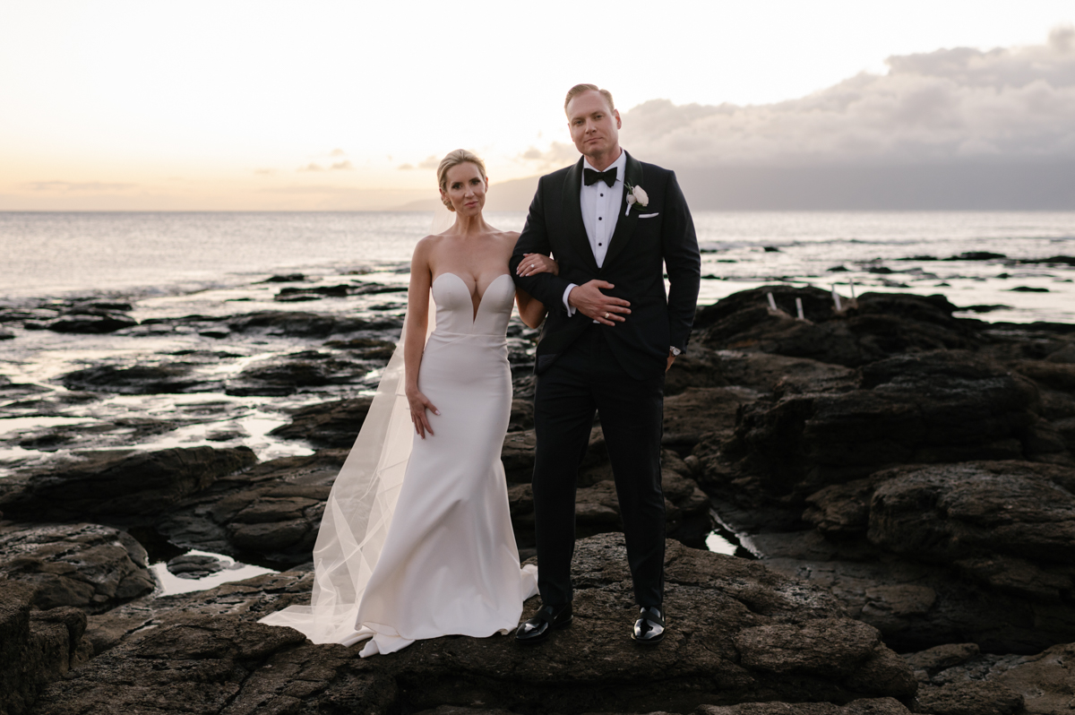 Bride and groom standing together on the lava rocks at sunset in Kapalua, Maui with the ocean behind them.
