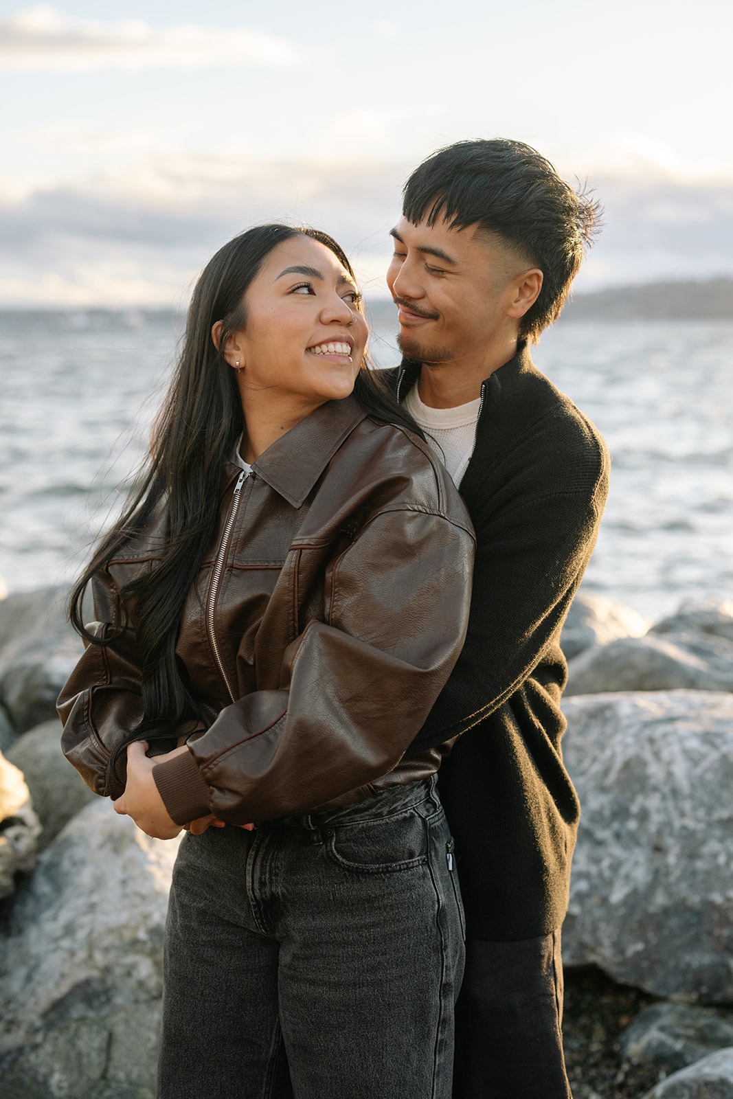 Seattle beach engagement portrait of newly engaged couple laughing on the rocky shore at Pocket Beach