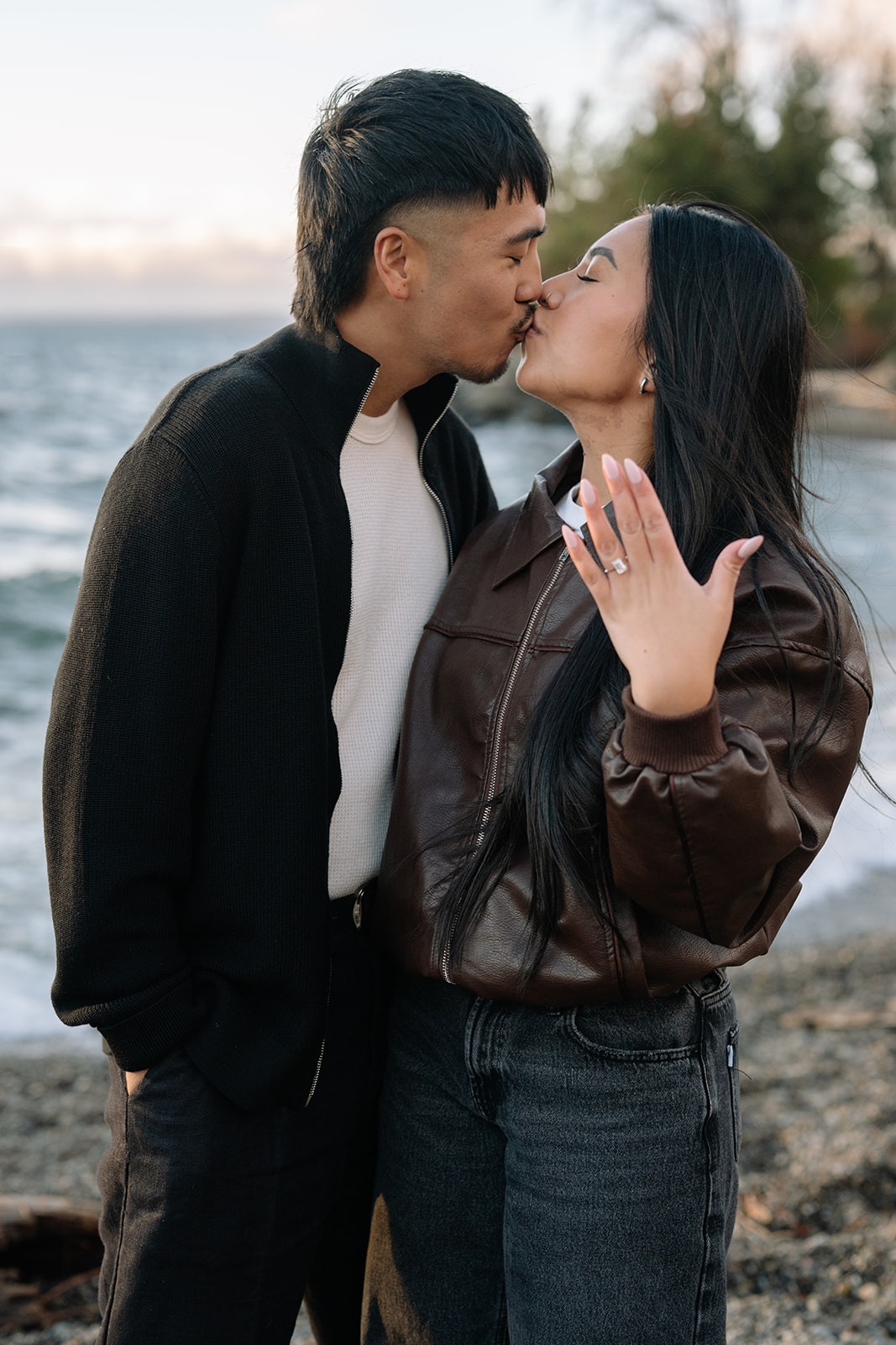Kiss between newly engaged couple as she holds up her ring at a Seattle beach proposal