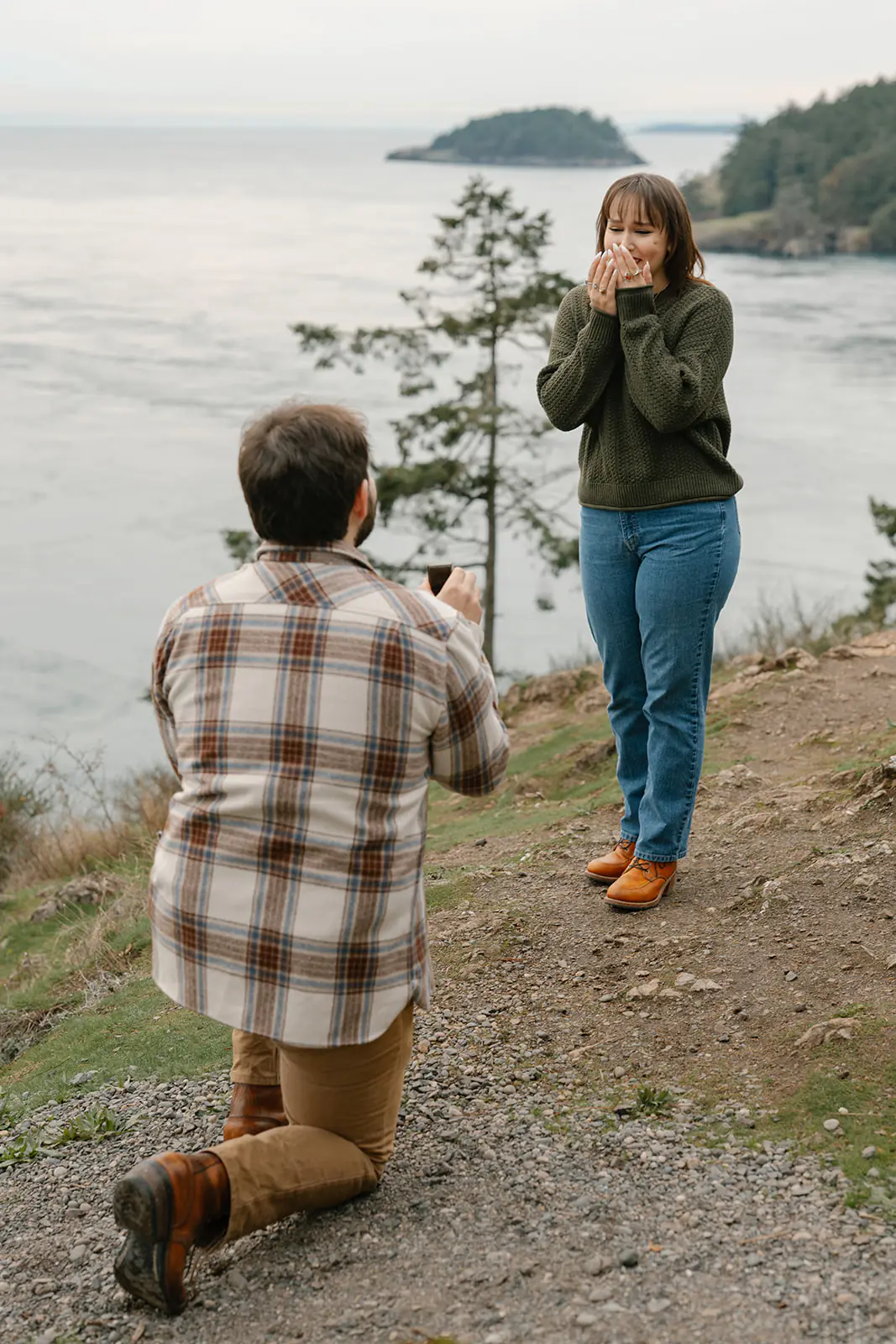 Ashley covers her mouth in surprise and emotion as Jonathan proposes by the water.