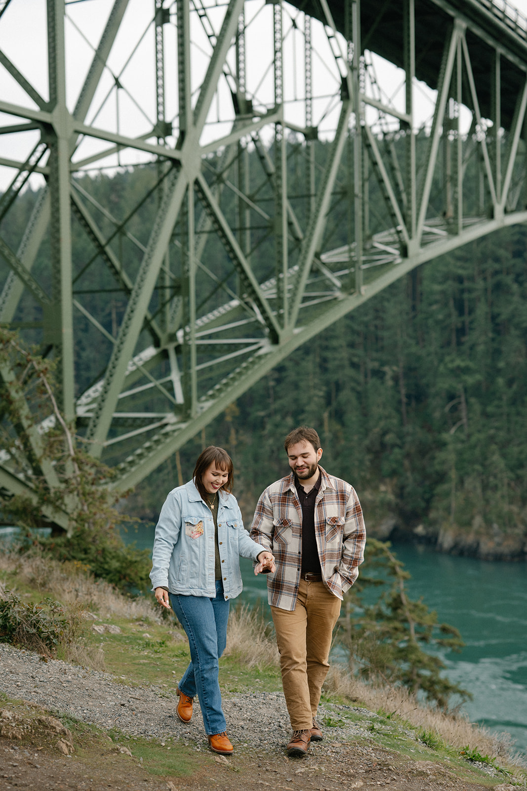 Jonathan and Ashley walk together beneath the Deception Pass Bridge, holding hands after their engagement.

