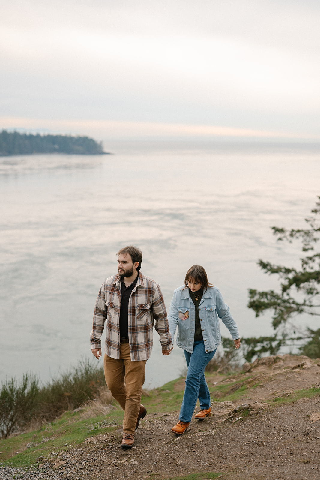 Jonathan and Ashley walk hand in hand along a coastal trail overlooking the water at Deception Pass.