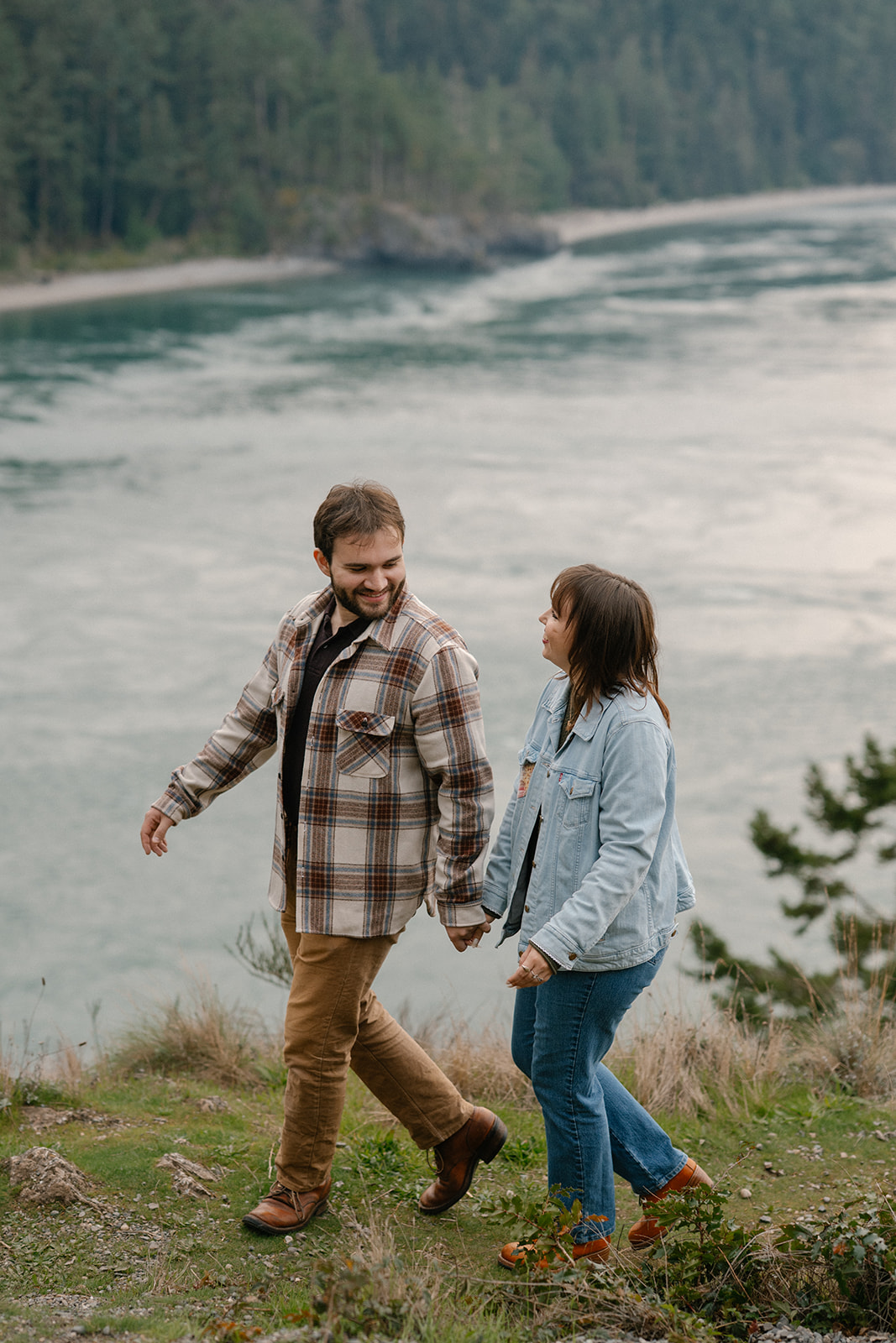 Jonathan and Ashley smile at each other while walking along the bluff with ocean views behind them.