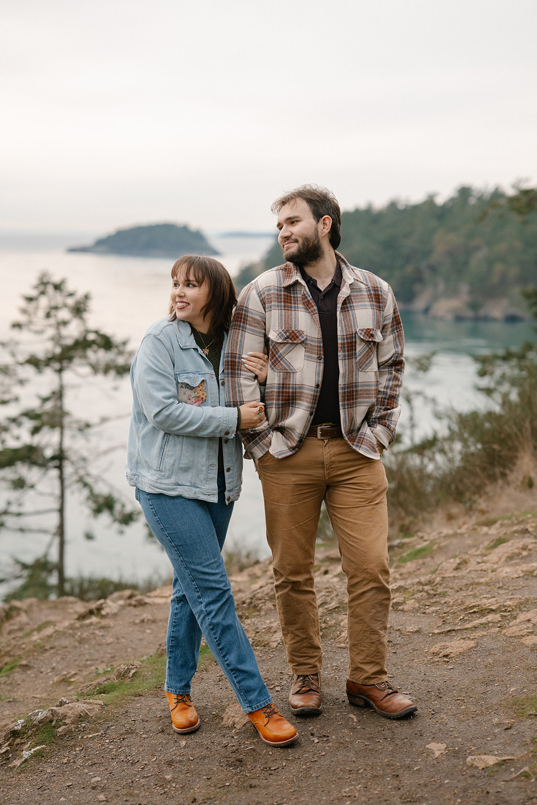 Jonathan and Ashley stand close together on the cliffside overlooking the water at Deception Pass.
