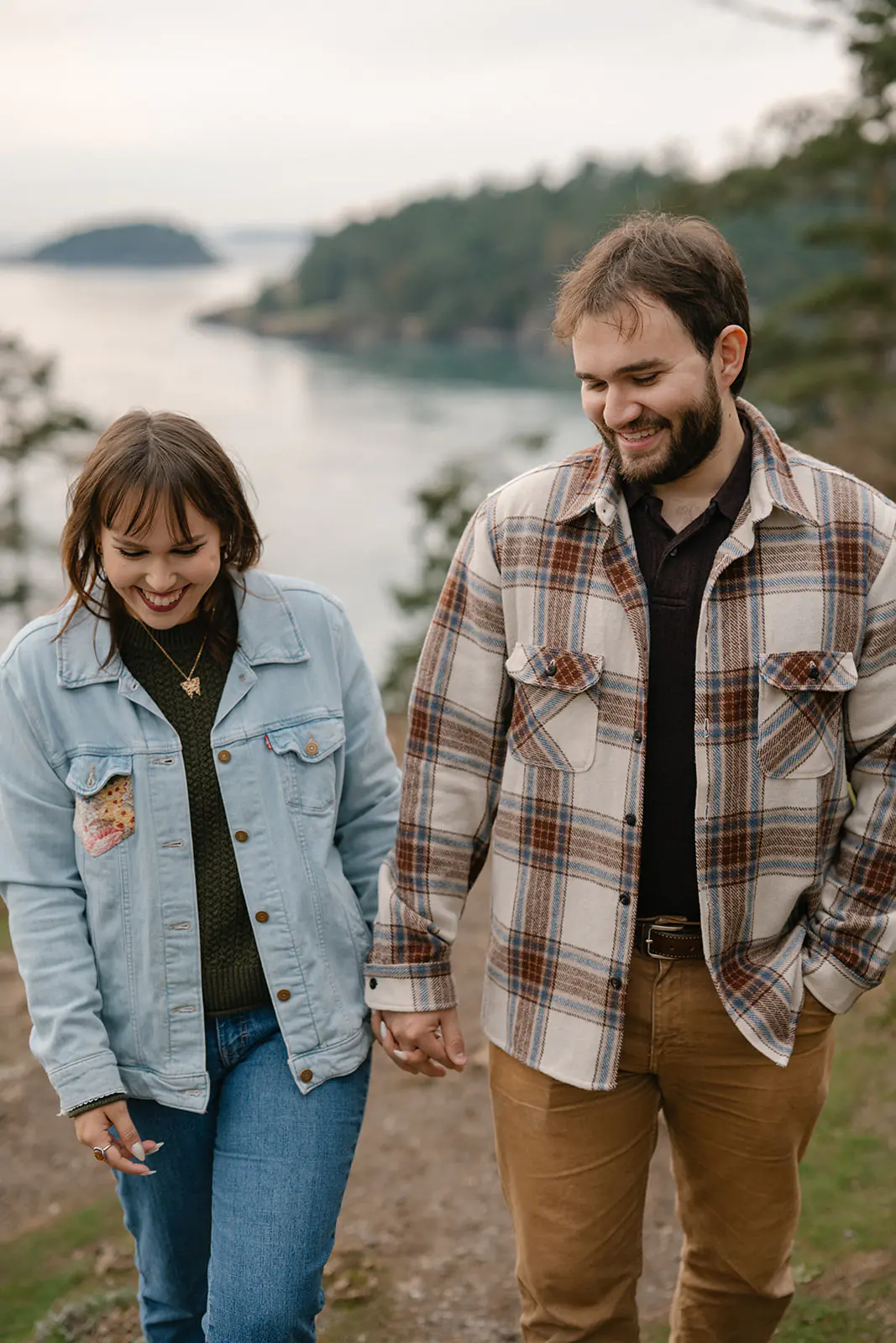 Jonathan and Ashley walk hand in hand along the trail at Deception Pass, smiling after their proposal.
