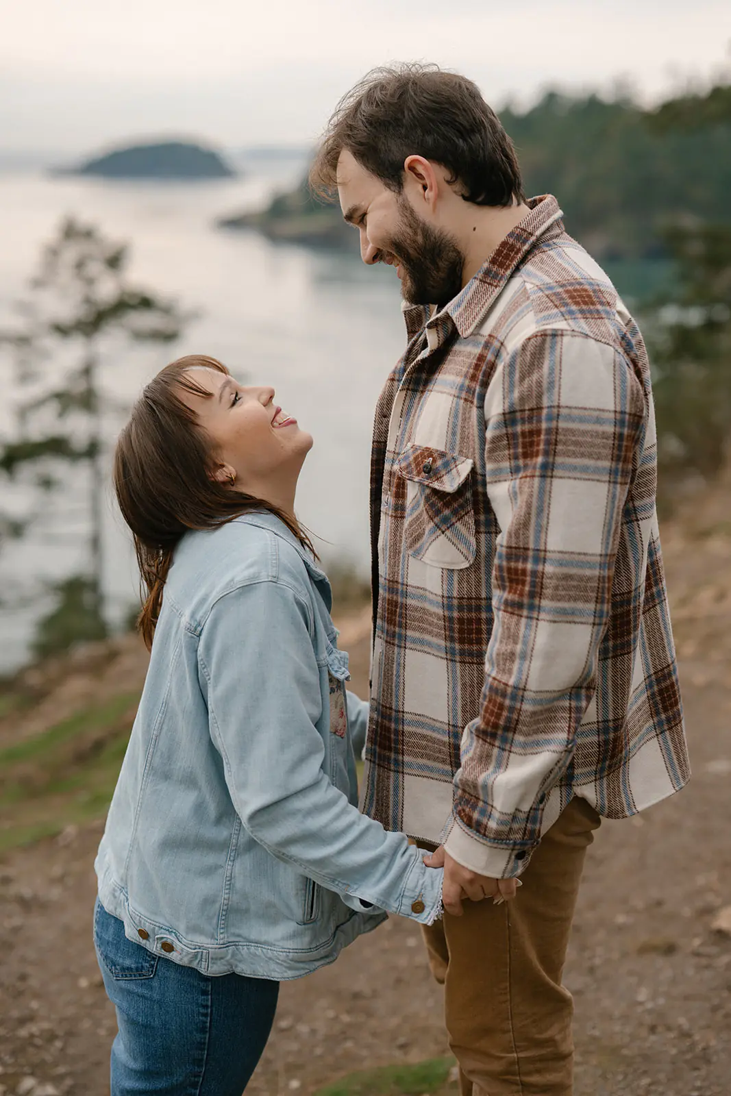 Ashley looks up at Jonathan while they hold hands on the cliff overlooking the water at Deception Pass.
