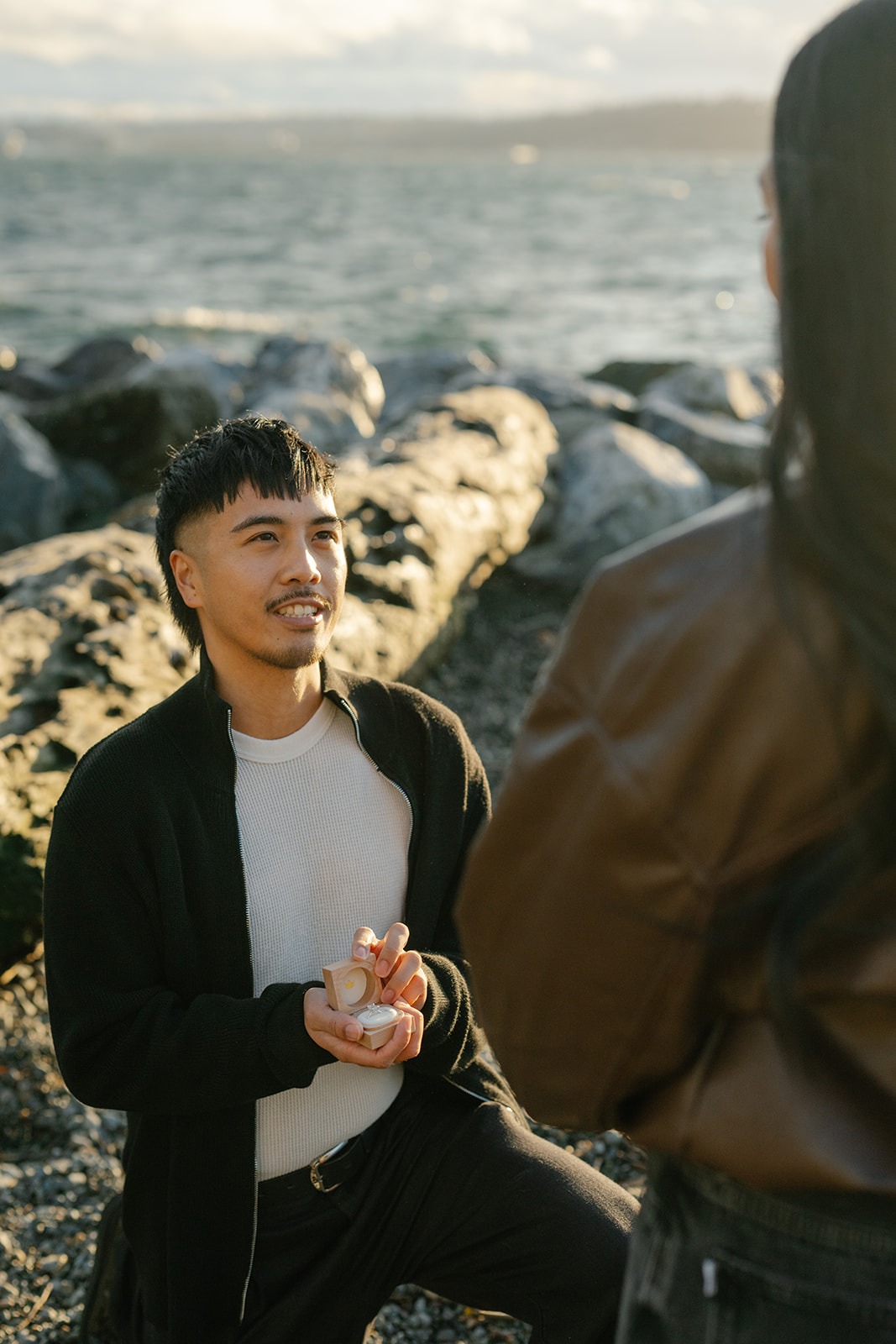 Fiancé-to-be smiles as he opens the ring box during a surprise beach proposal in Seattle