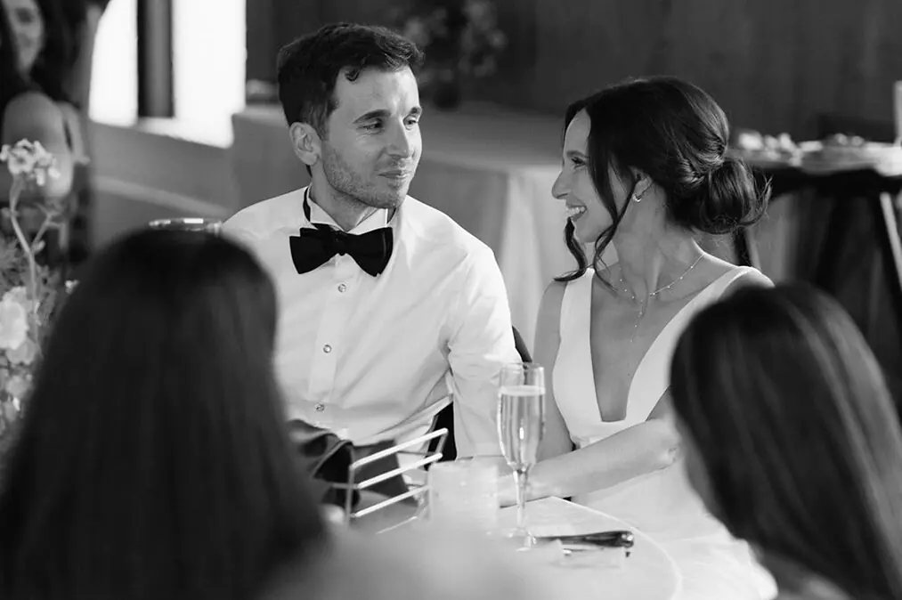 Bride and groom smiling at each other while seated during toasts at their Fremont Foundry wedding