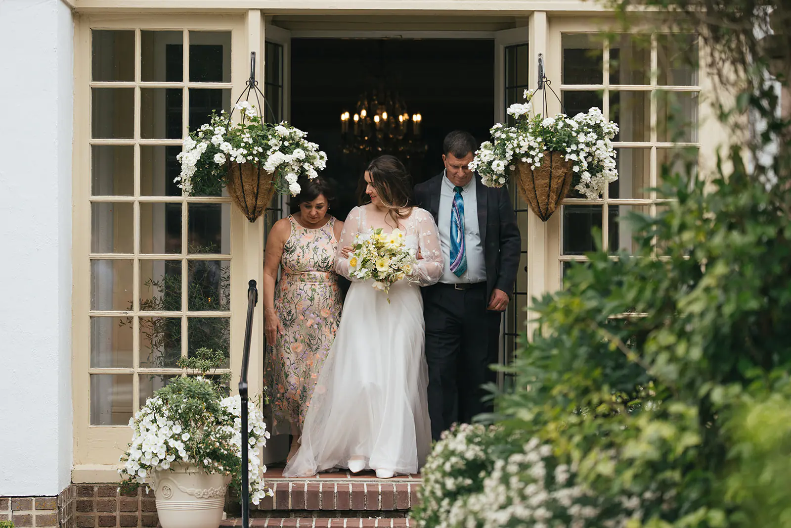 Bride walking with her parents through garden doors before ceremony at Lairmont Manor wedding