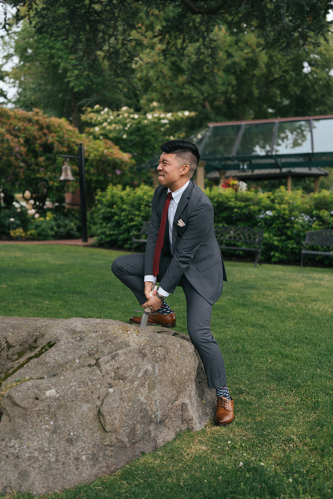 Groomsmen playfully attempting to pull a sword from a stone on the lawn at Lairmont Manor