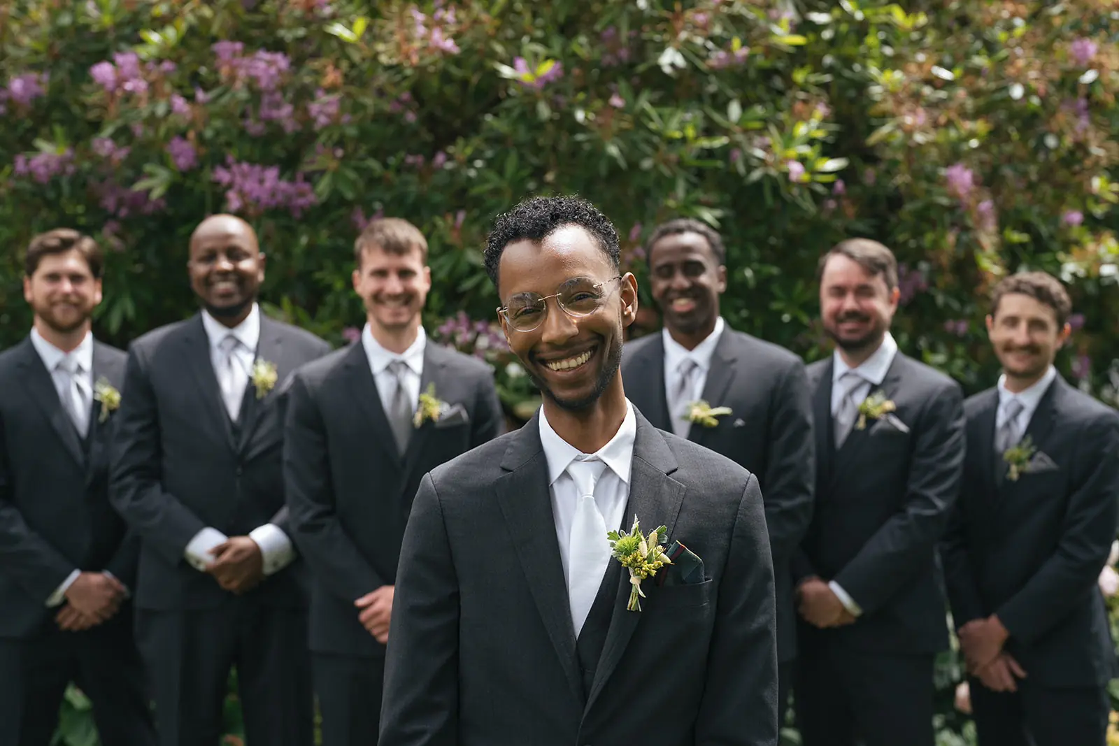 Groom smiling with his groomsmen standing together in the garden.