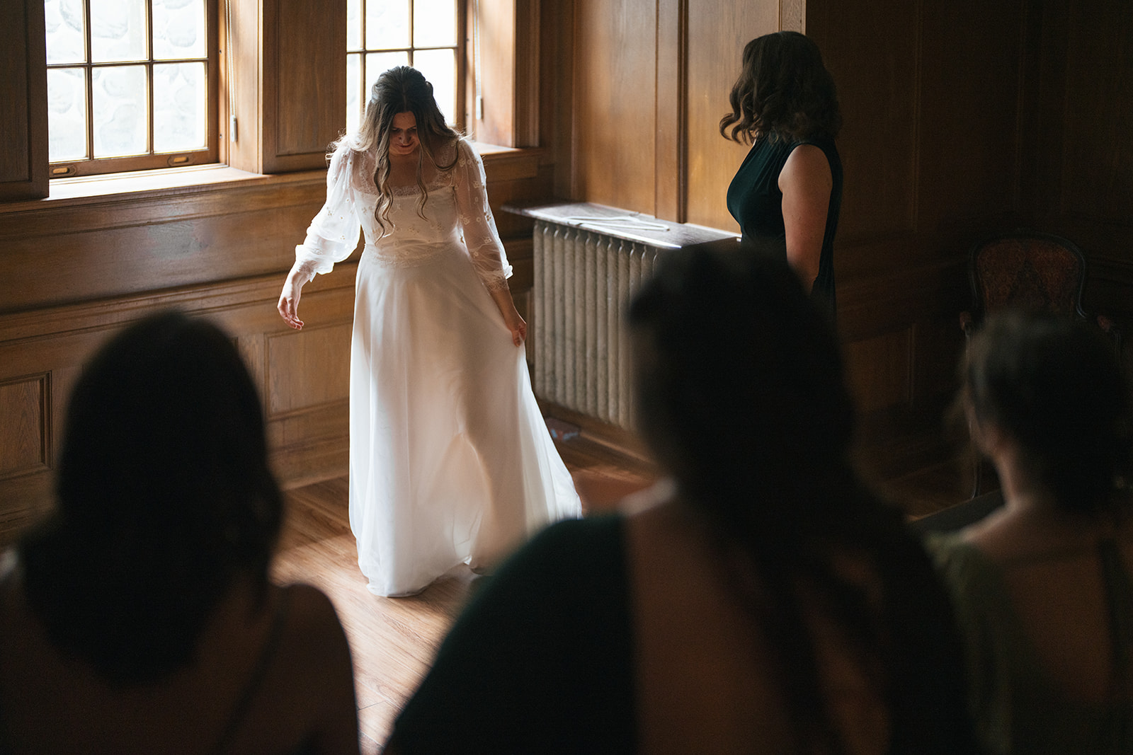 Bride standing in her gown while bridesmaids watch during wedding preparations