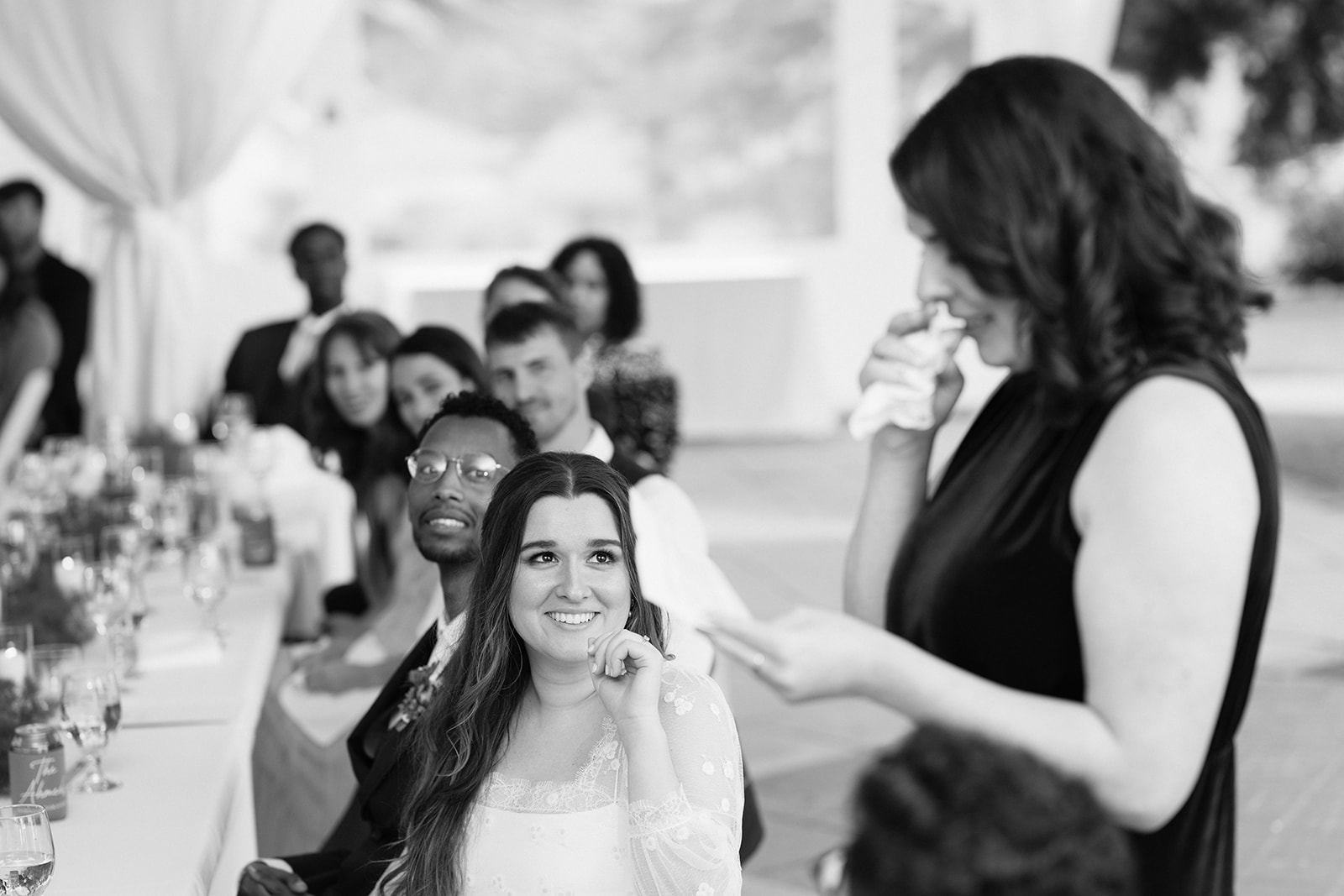Bride smiling at a speaker while seated at the head table during the tent reception at Lairmont Manor