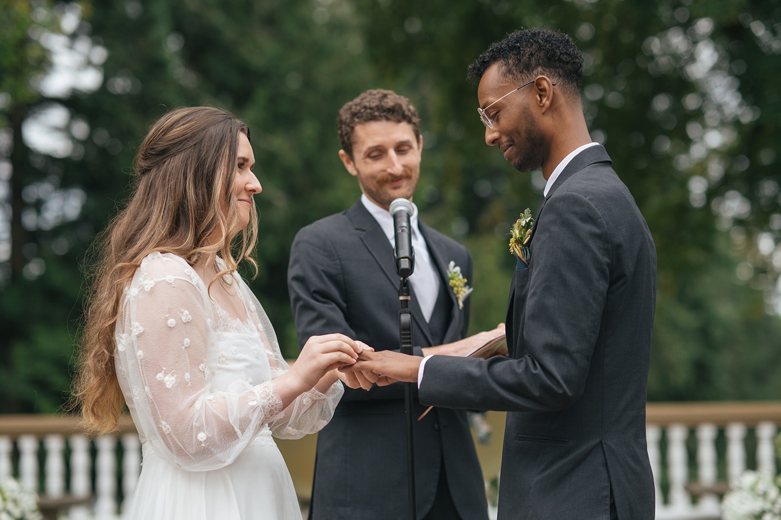 Bride placing ring on groom’s finger during wedding ceremony while friend officiates