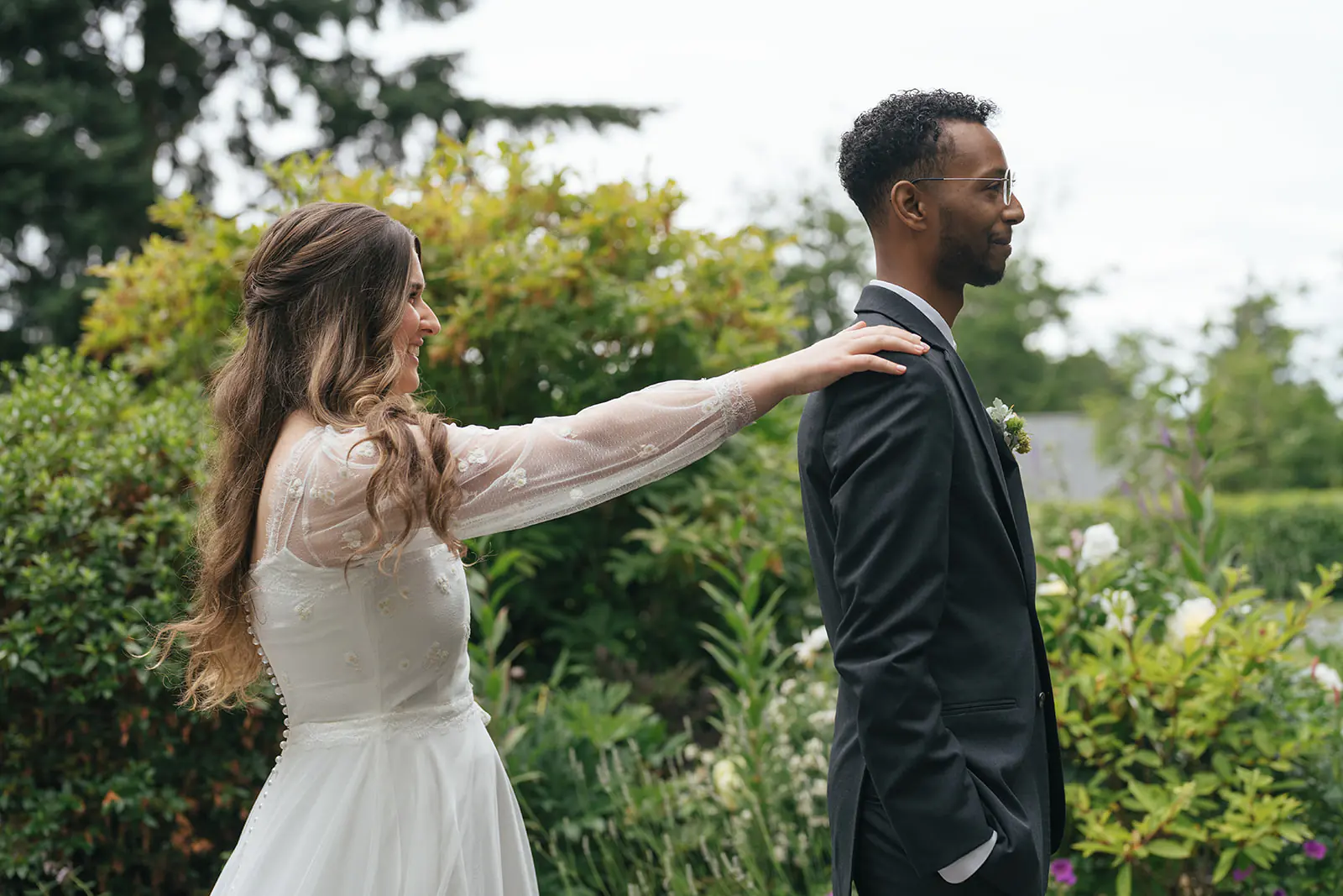 Bride taps groom on the shoulder during an emotional garden first look at Lairmont Manor in Bellingham Washington.
